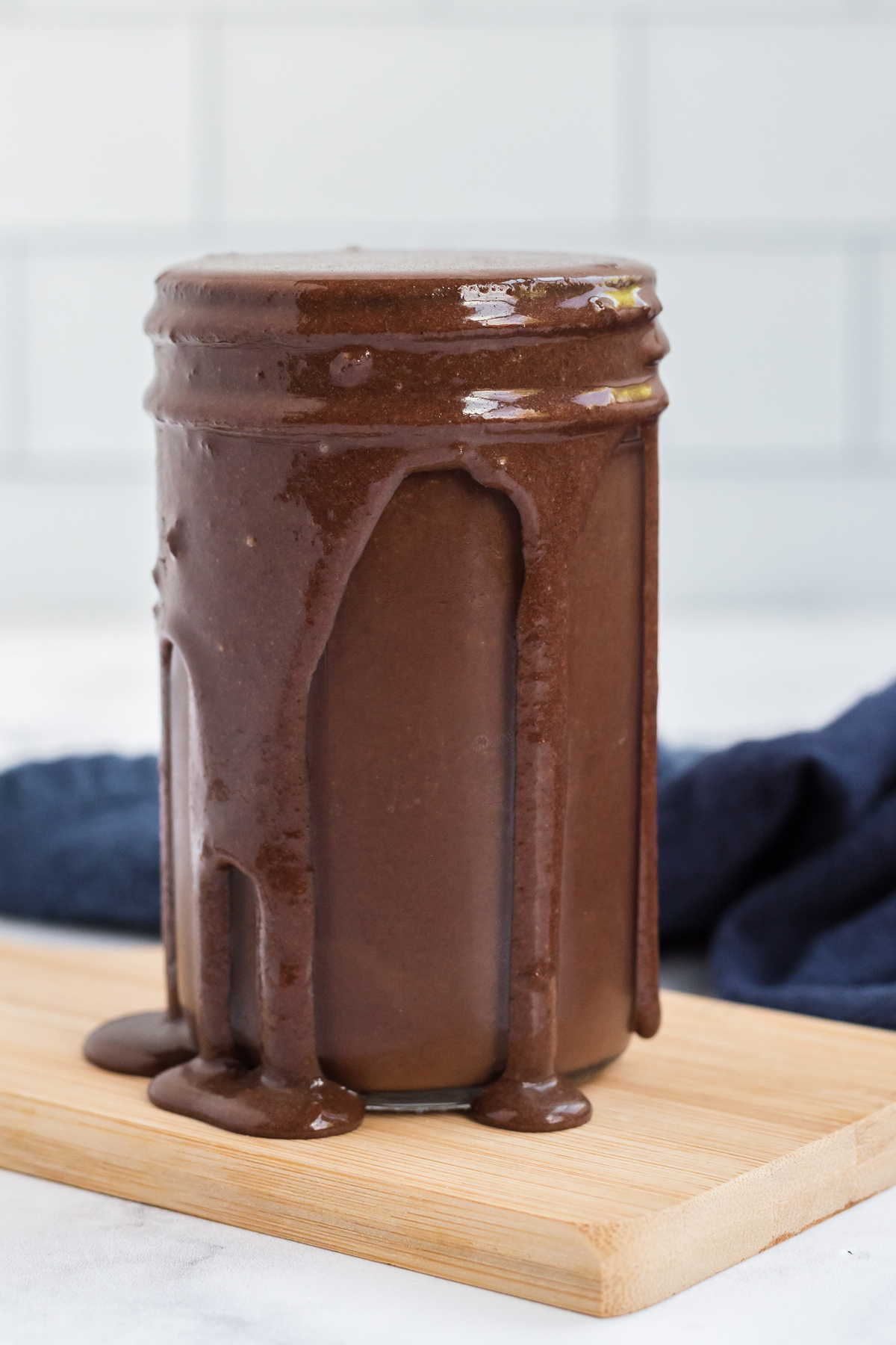 Hot fudge sauce on a jar with a wooden board and a linen in background