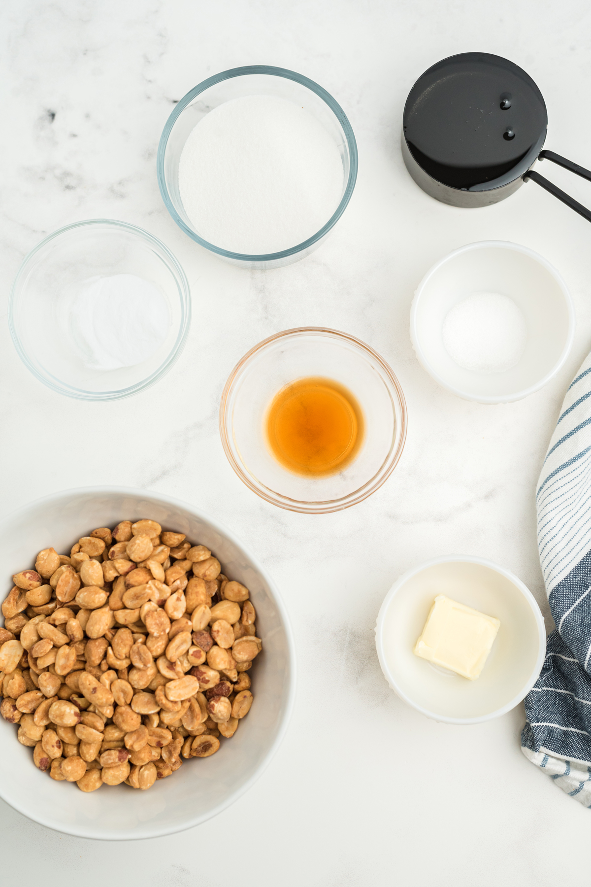 Flatlay of peanut brittle ingredients which includes peanuts, butter, vanilla, sugar, and corn syrup.