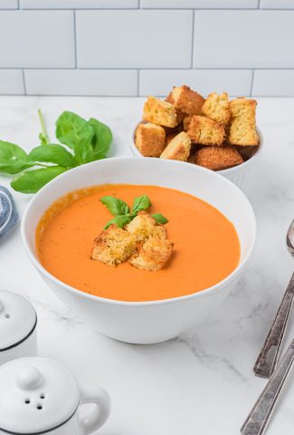 tomato soup in white bowl with croutons and fresh basil