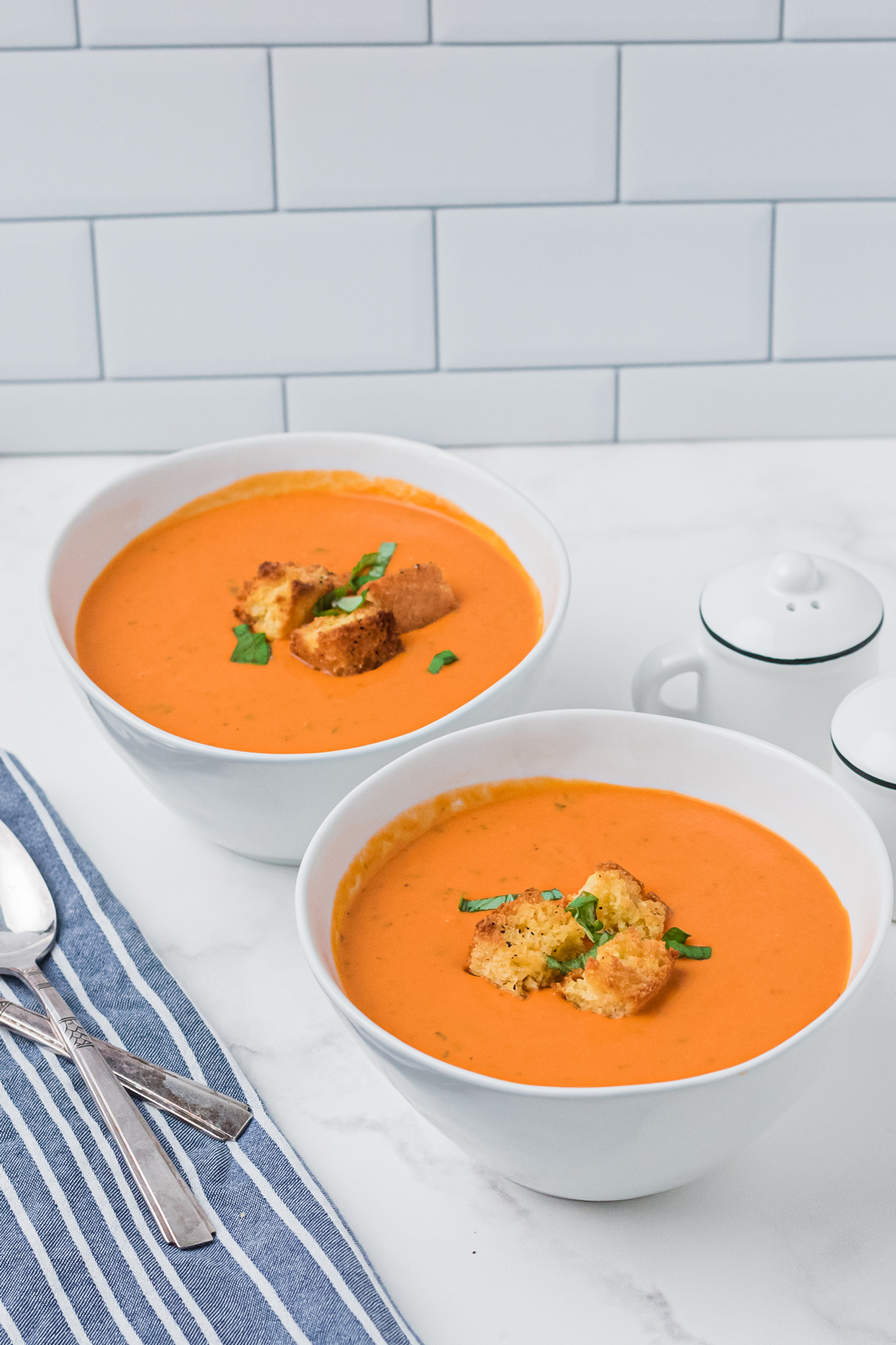 Two bowls of Tomato Soup on a white counter with utensils. 