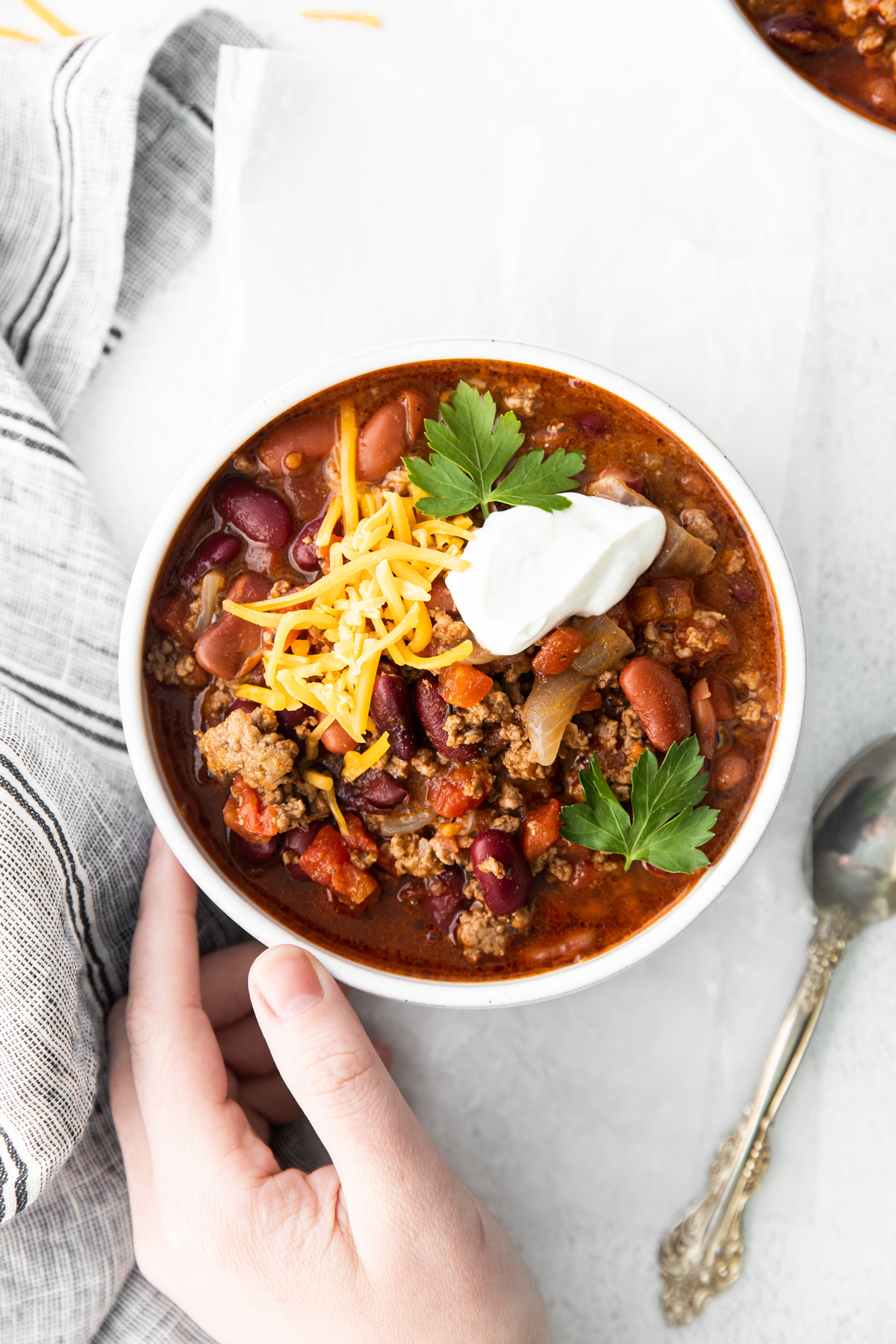 Slow cooker chili on a bowl with a hand and spoon on side.