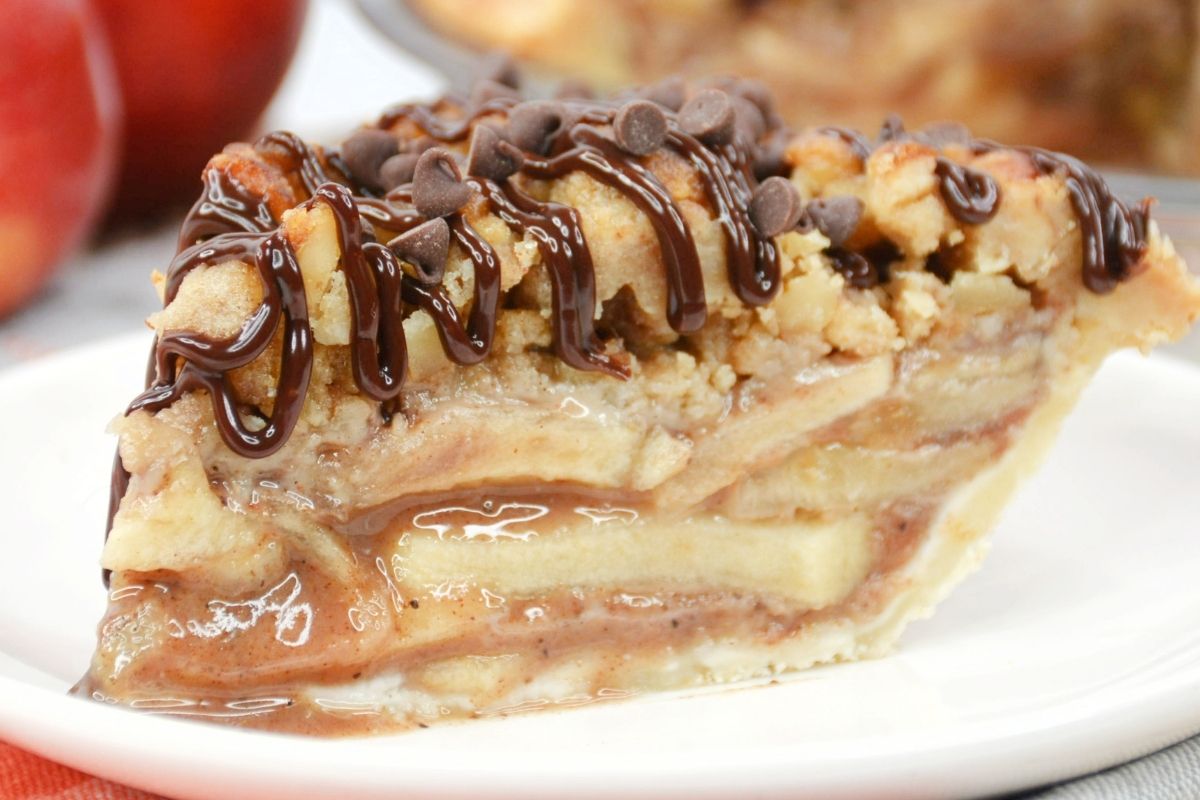 slice of apple crumble pie showing slices of apple and a chocolate drizzle on top