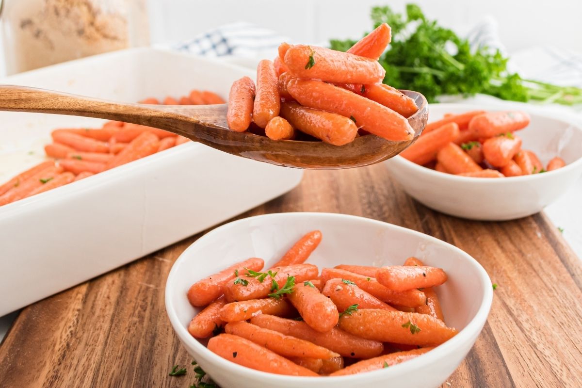 wooden spoon with baby carrots and a bowl of baked baby carrots