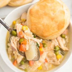 chicken pot pie on spoon with bowl and biscuit