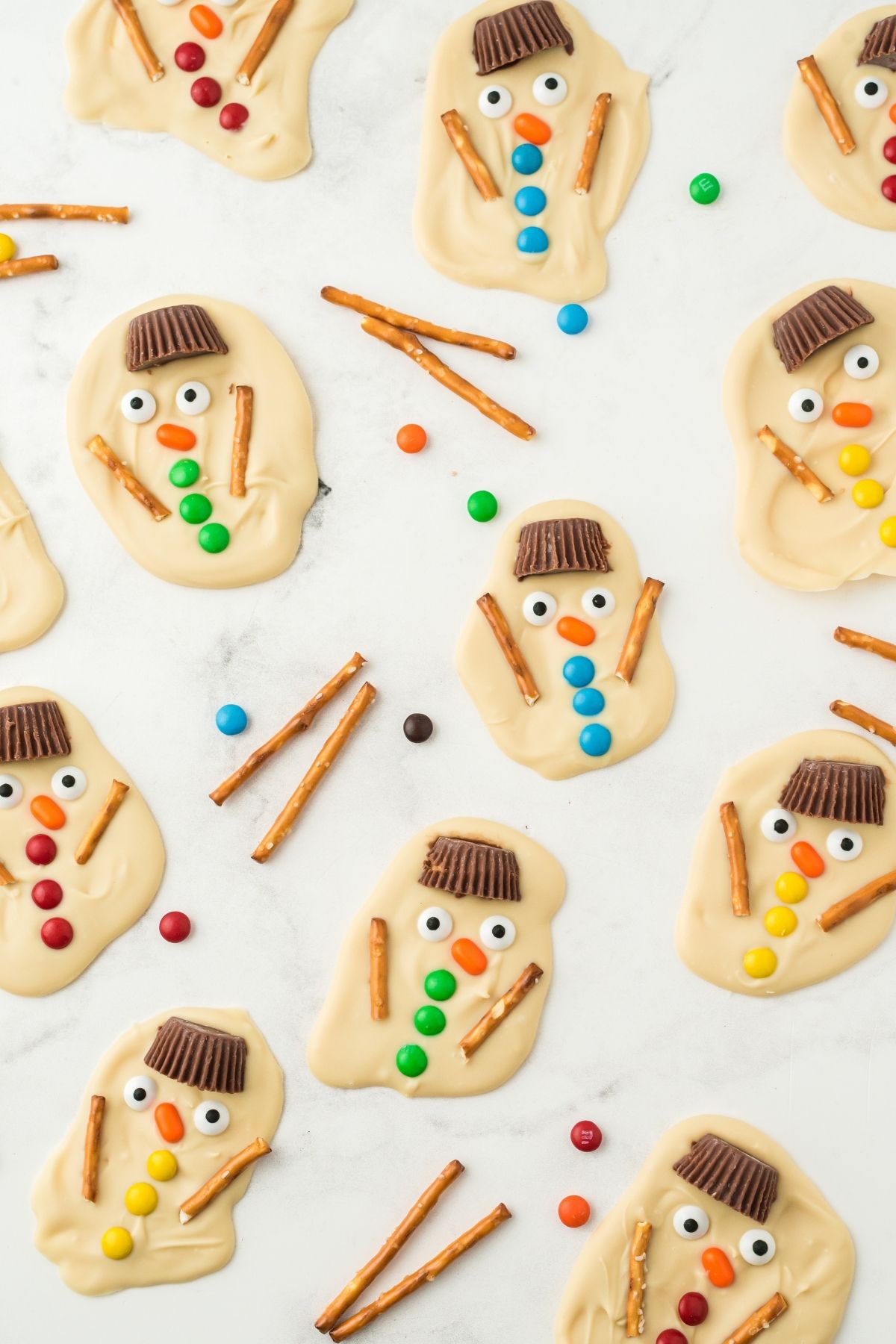white chocolate snowman with colored buttons and pretzel sticks for arms on counter