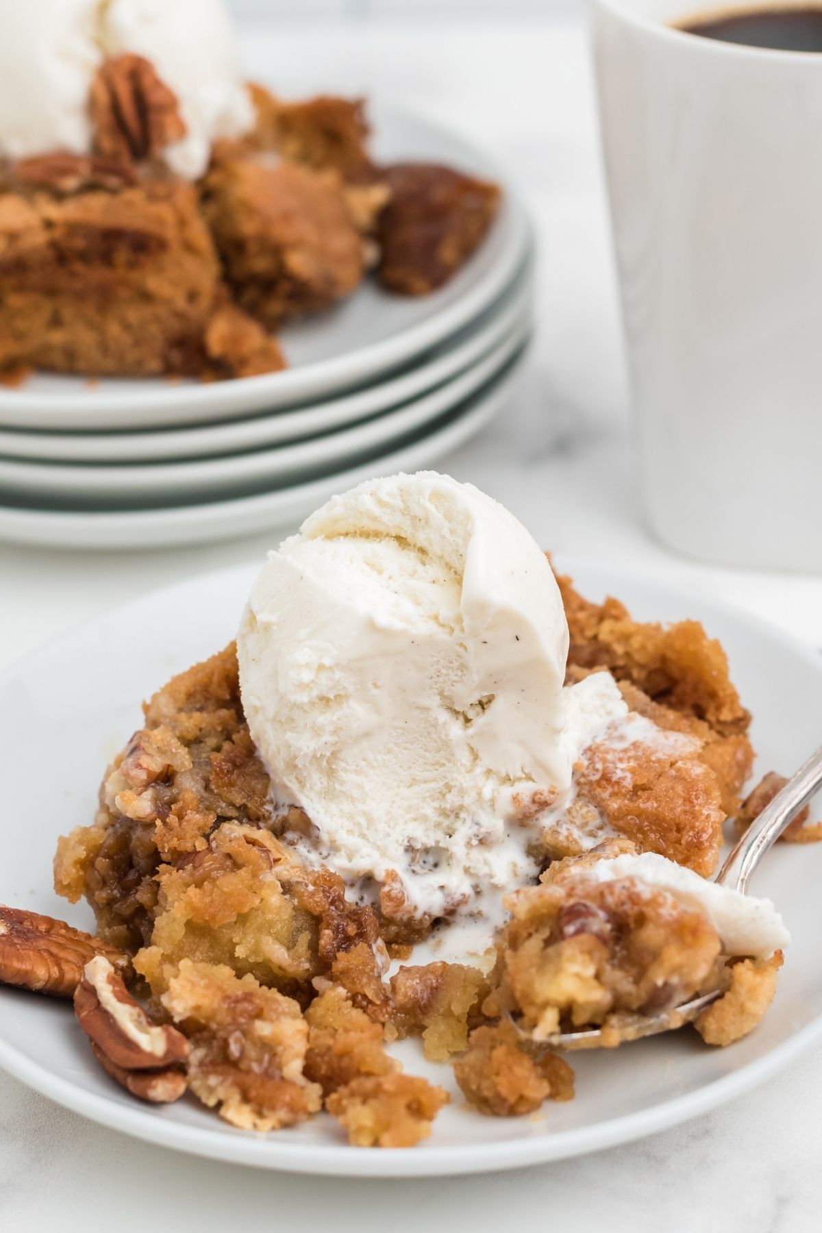 pecan dump cake with ice cream on top with plates and a cup of coffee