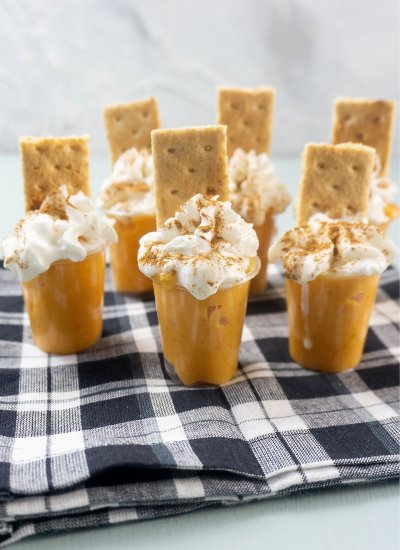 small shot glasses with pumpkin pudding topped with whipped cream and a graham cracker