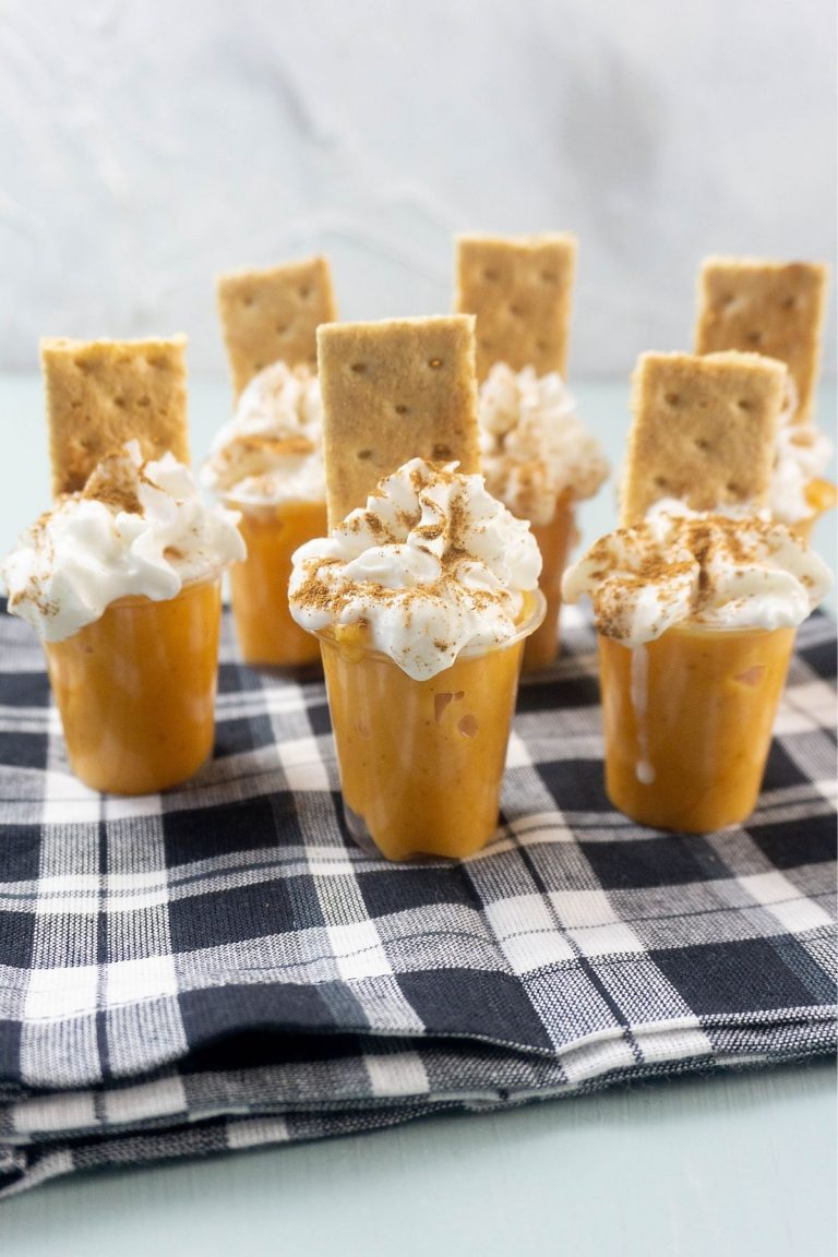 small shot glasses with pumpkin pudding topped with whipped cream and a graham cracker