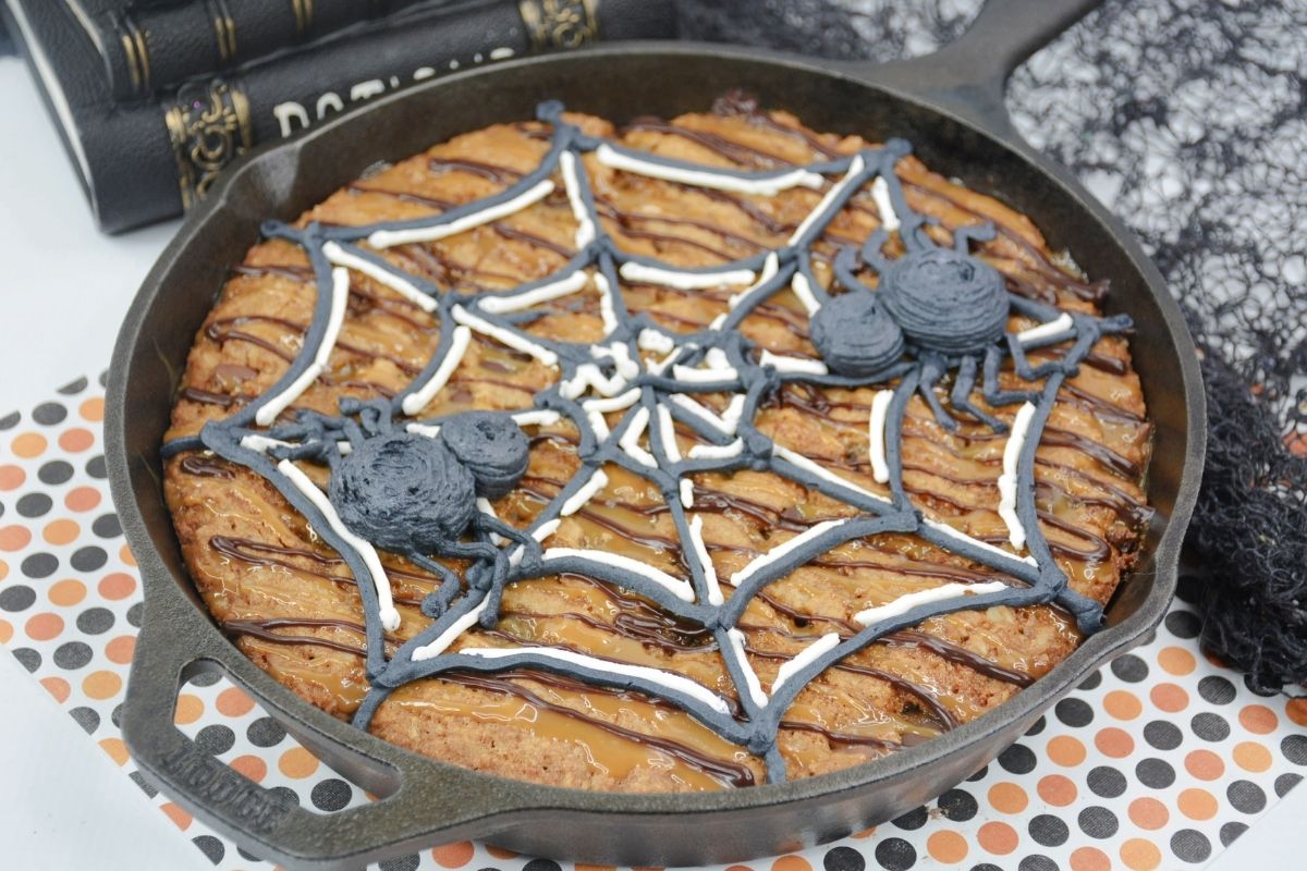 cookie in cast iron skillet with buttercream spider web and spiders