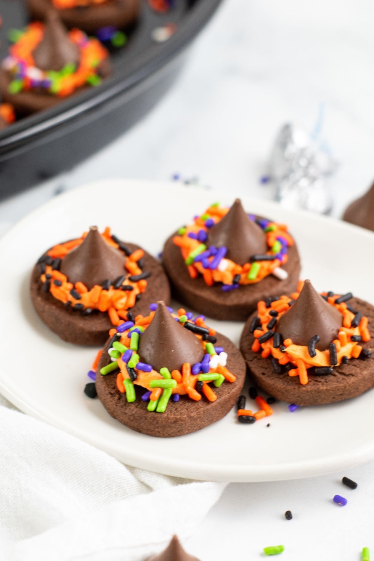 four chocolate cookies with geen, orange, and purple sprinkles with hershey's kiss on top