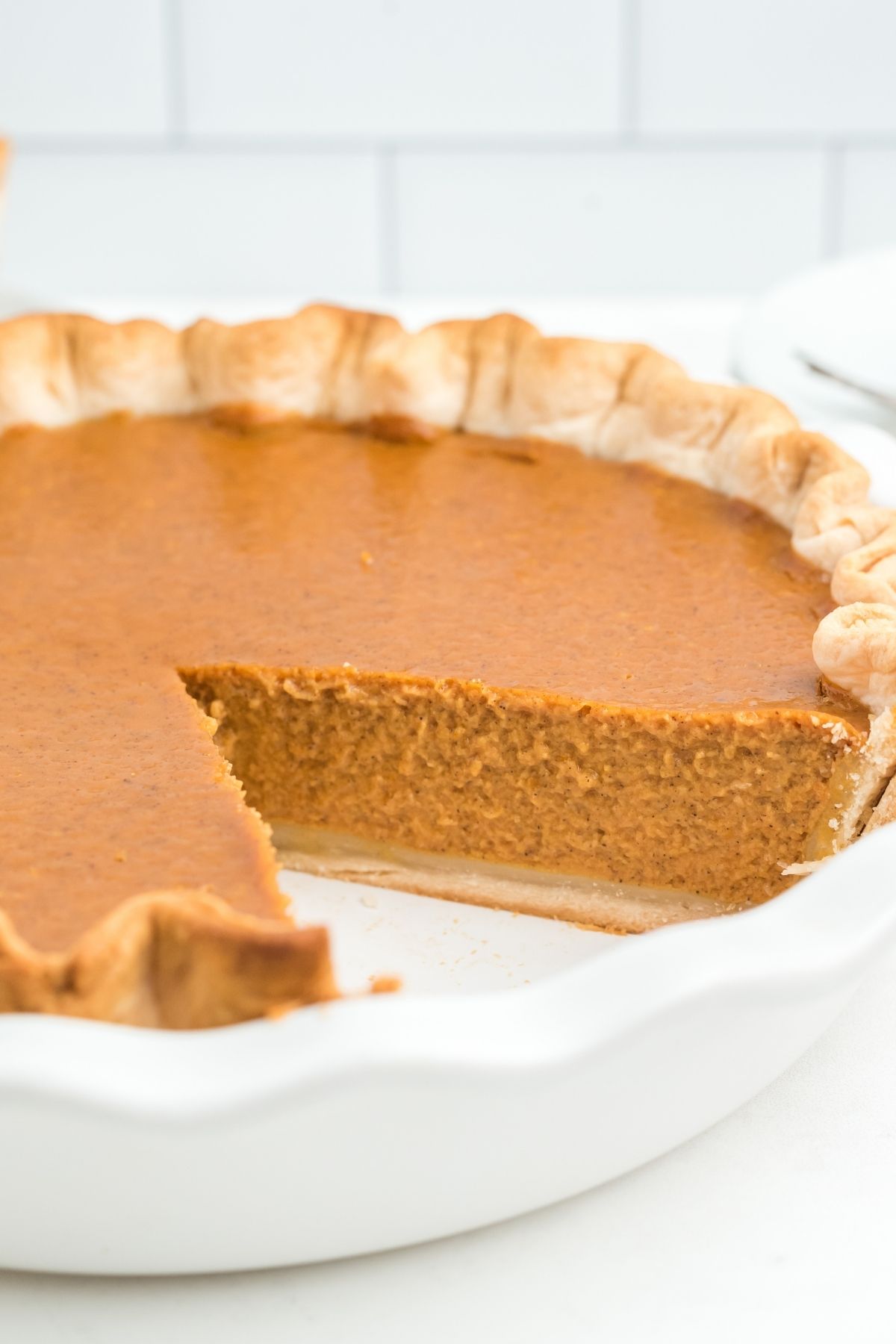 whole pumpkin pie with a slice cut out showing a thick pumpkin filling inside