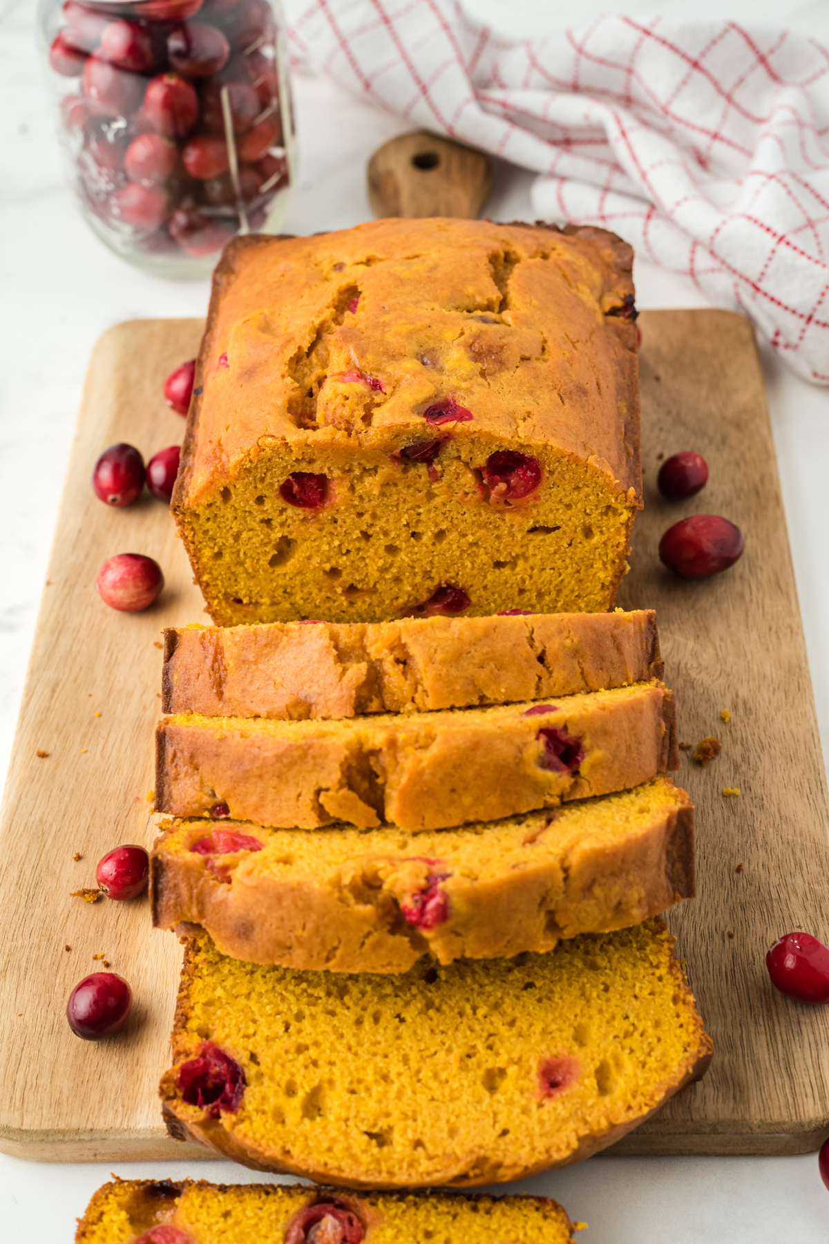 A sliced loaf of freshly baked Pumpkin Cranberry Bread on a wooden board. 