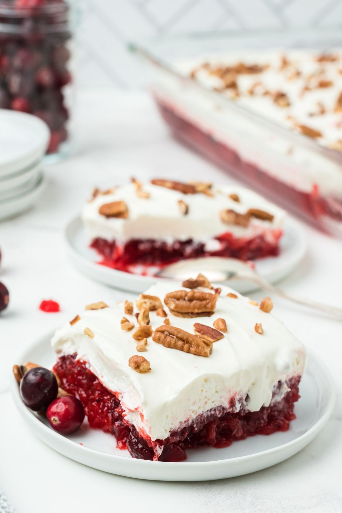 slice of cranberry jello salad with whipped cream layer on top with chopped pecans