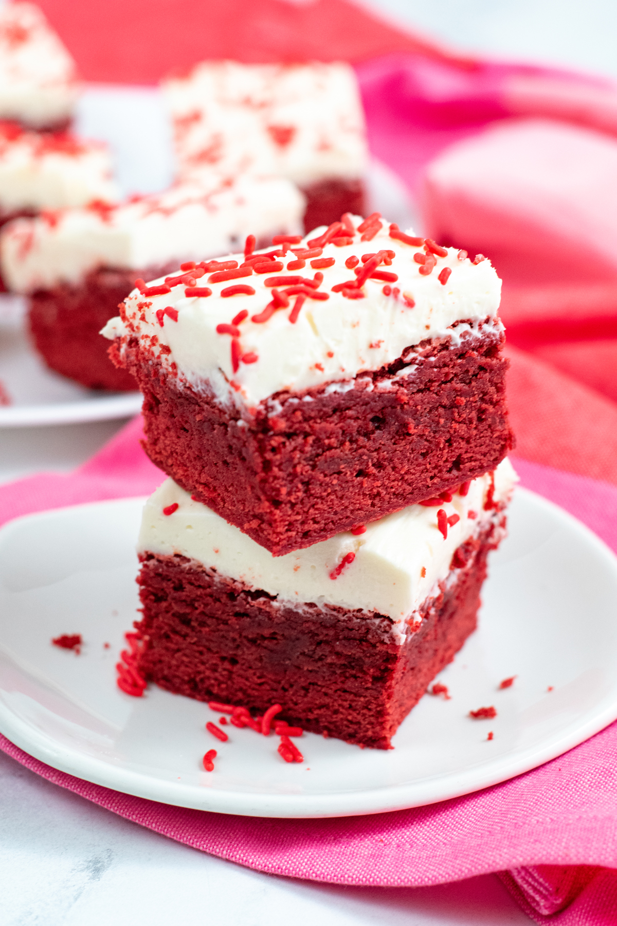 two red velvet brownies with white cream cheese frosting and red sprinkles
