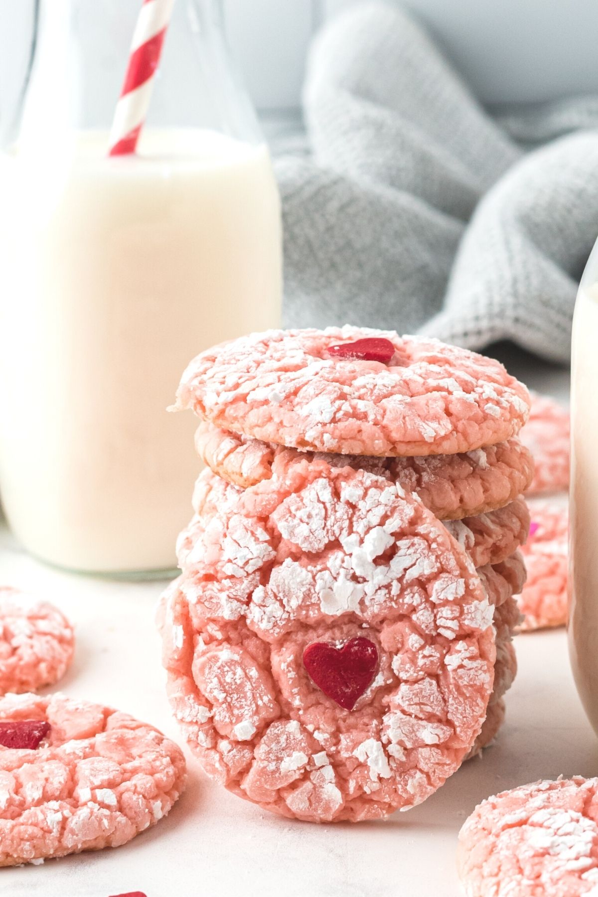 pink crinkle cookies with red heart in center next to glass of milk