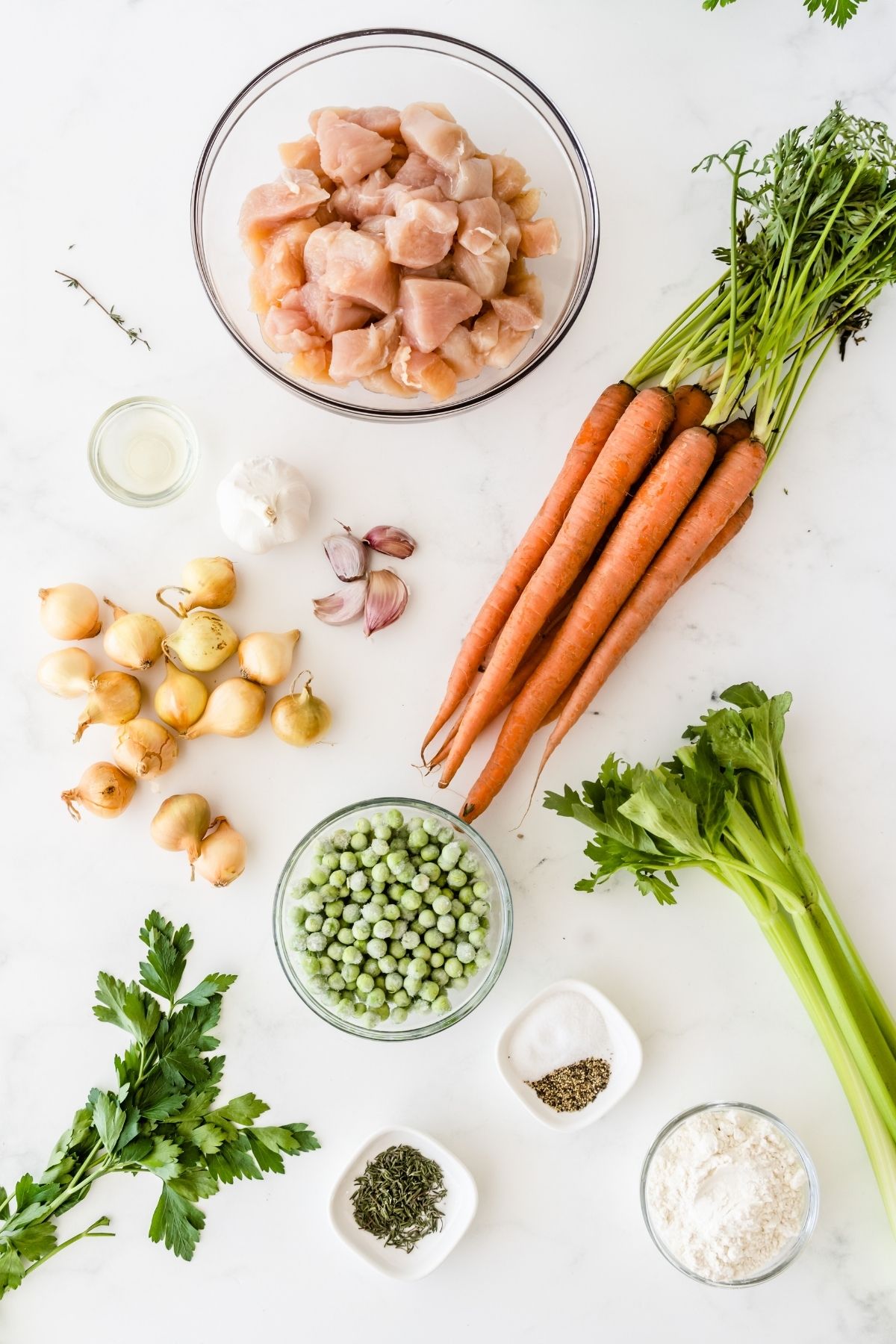 clear bowl with cubed chicken; carrots, garlic, shallots, celery, and frozen peas on white counter
