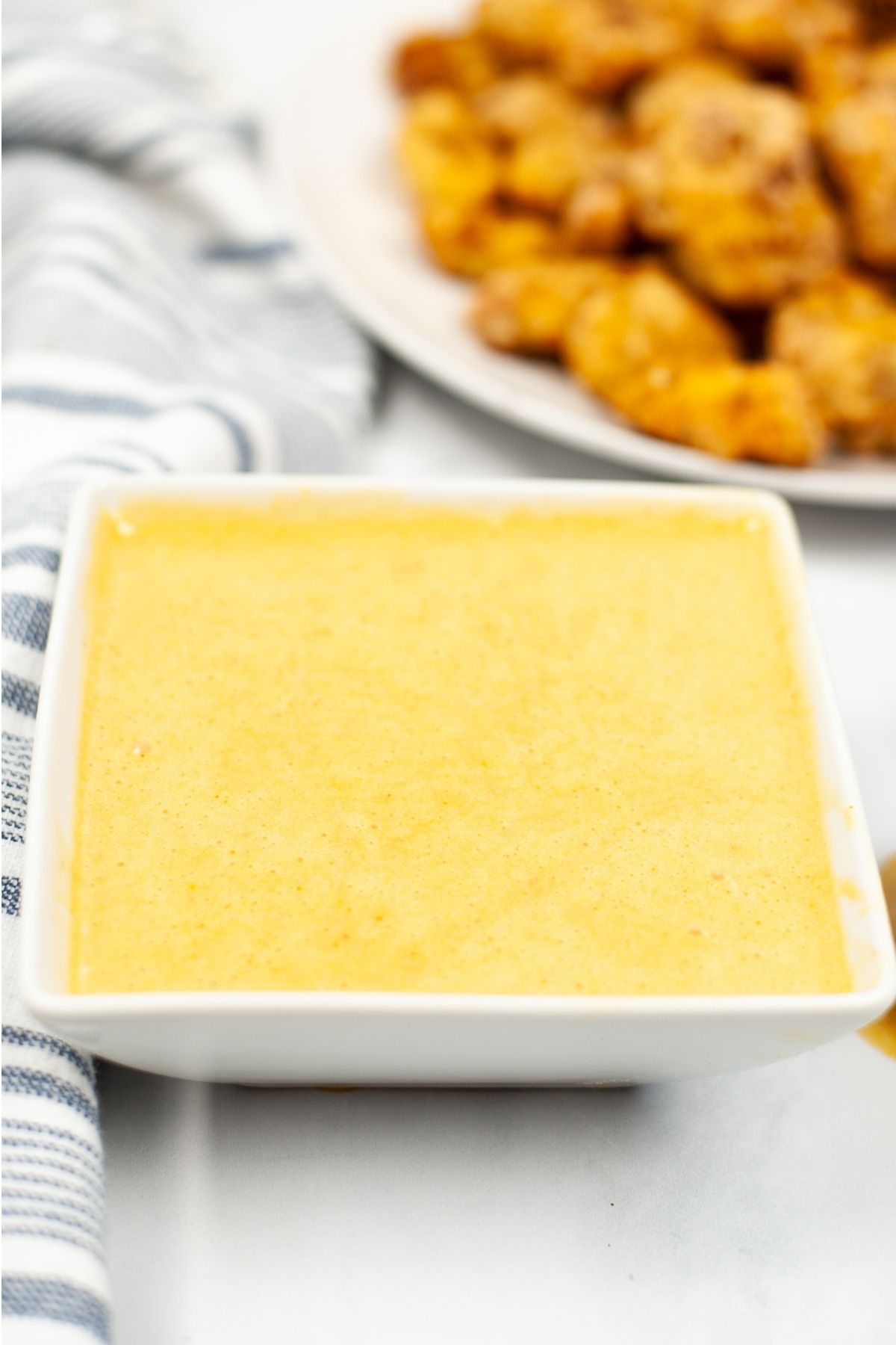 square bowl of yellow Chick-fil-a sauce with plate of Chick-fil-a nuggets on the side