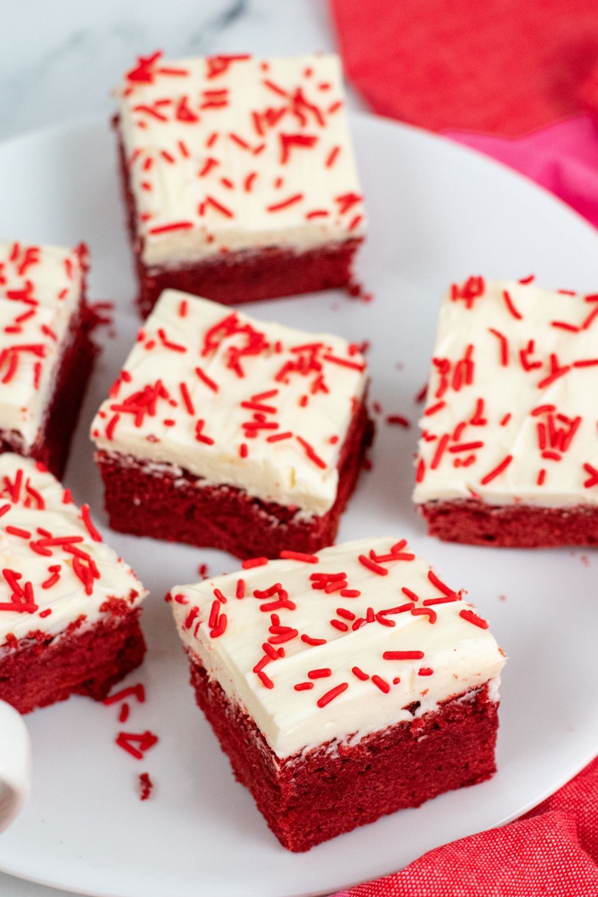 6 red brownies with white frosting and red sprinkles on a plate