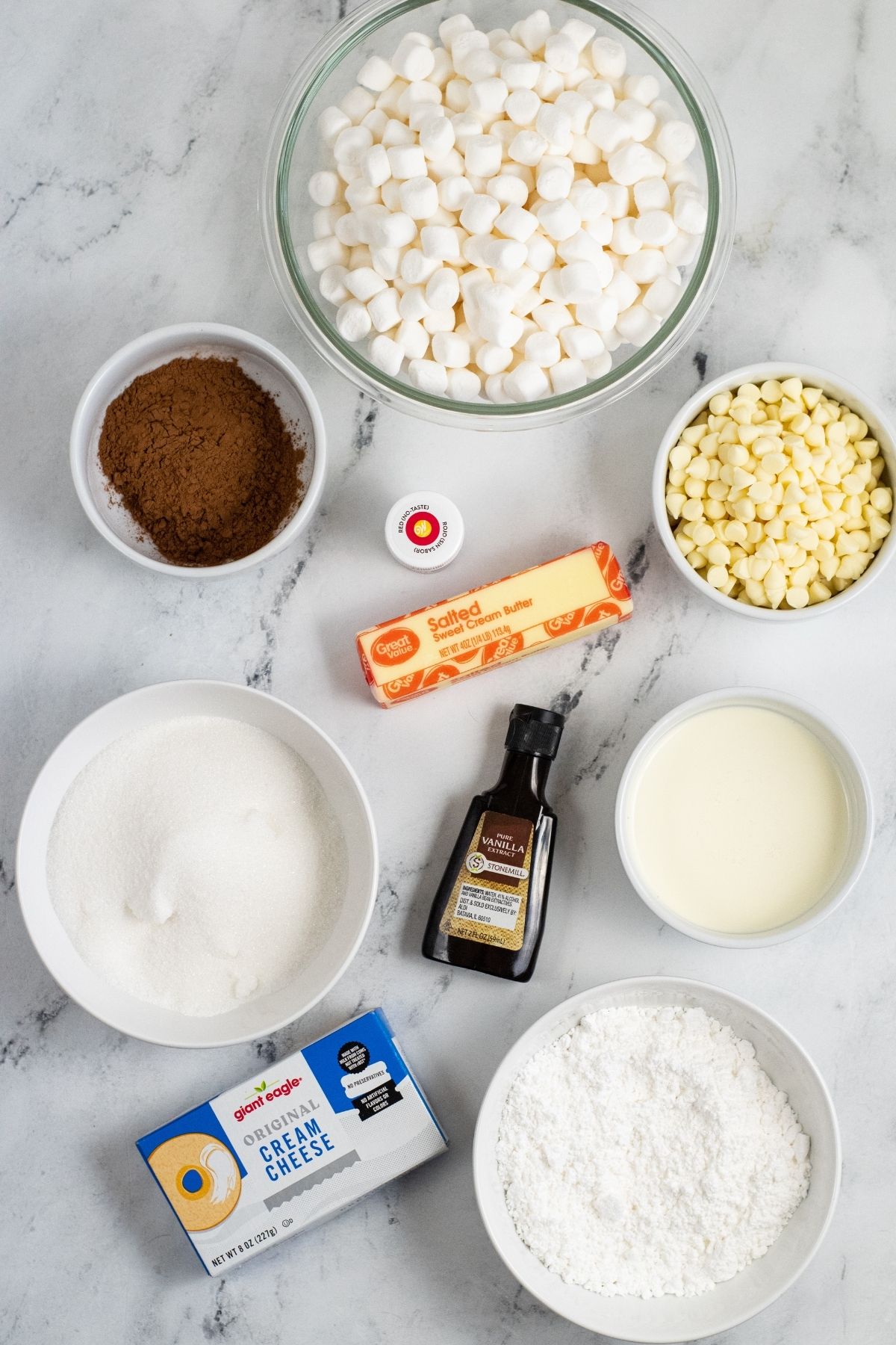 ingredients in bowls on white counter: mini marshmallows, white chocolate chips, 1 stick butter, red food coloring, cocoa powder, vanilla, cream cheese, sugar, powdered sugar