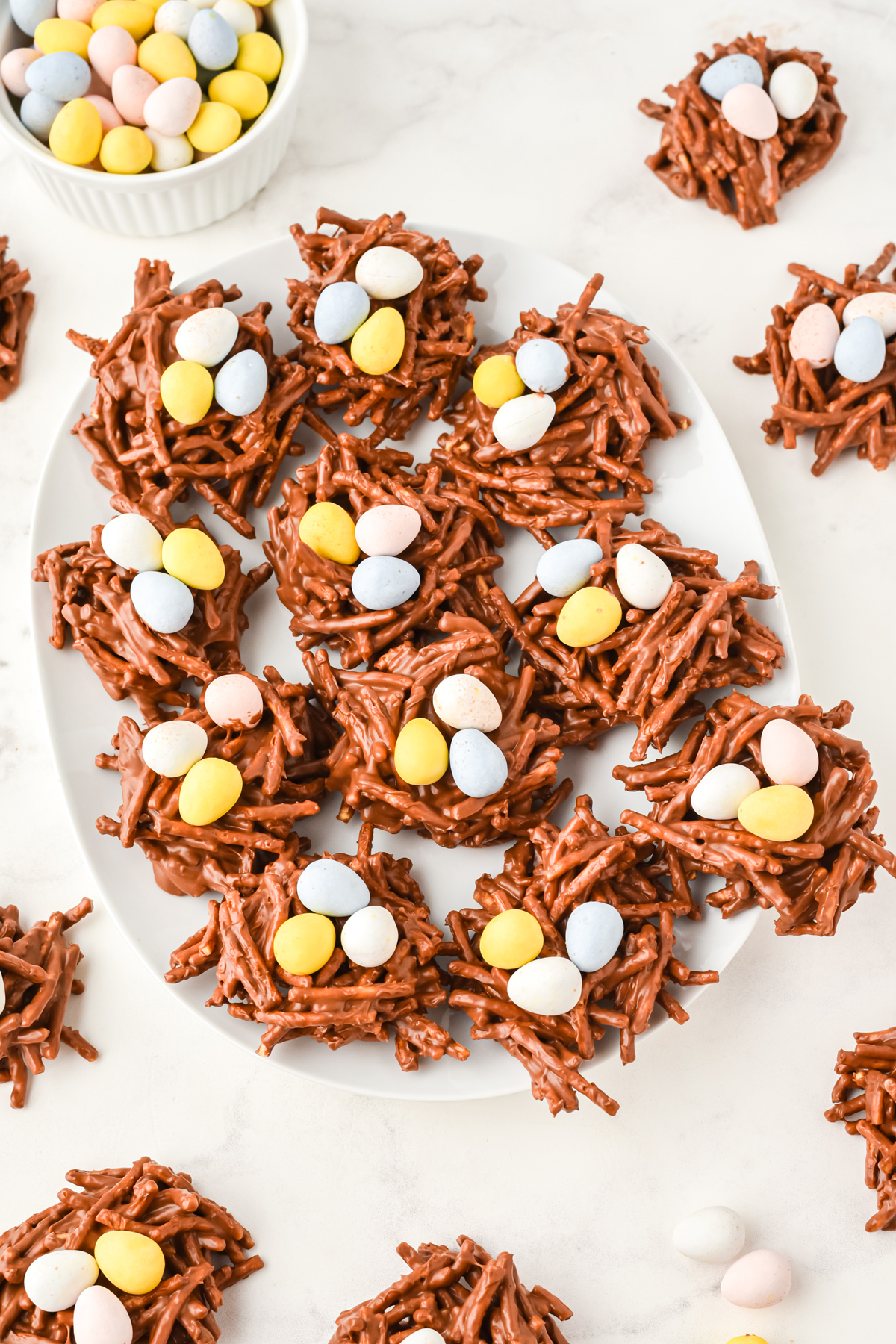 A plate of bird's nest cookies. Some are scattered on a white counter
