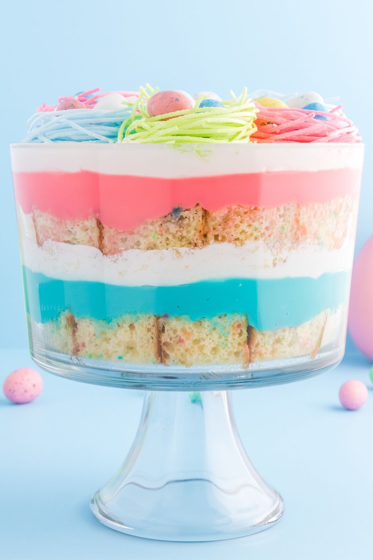 glass trifle bowl with layered funfetti cake mix with blue, white, and pink frosting in between layers