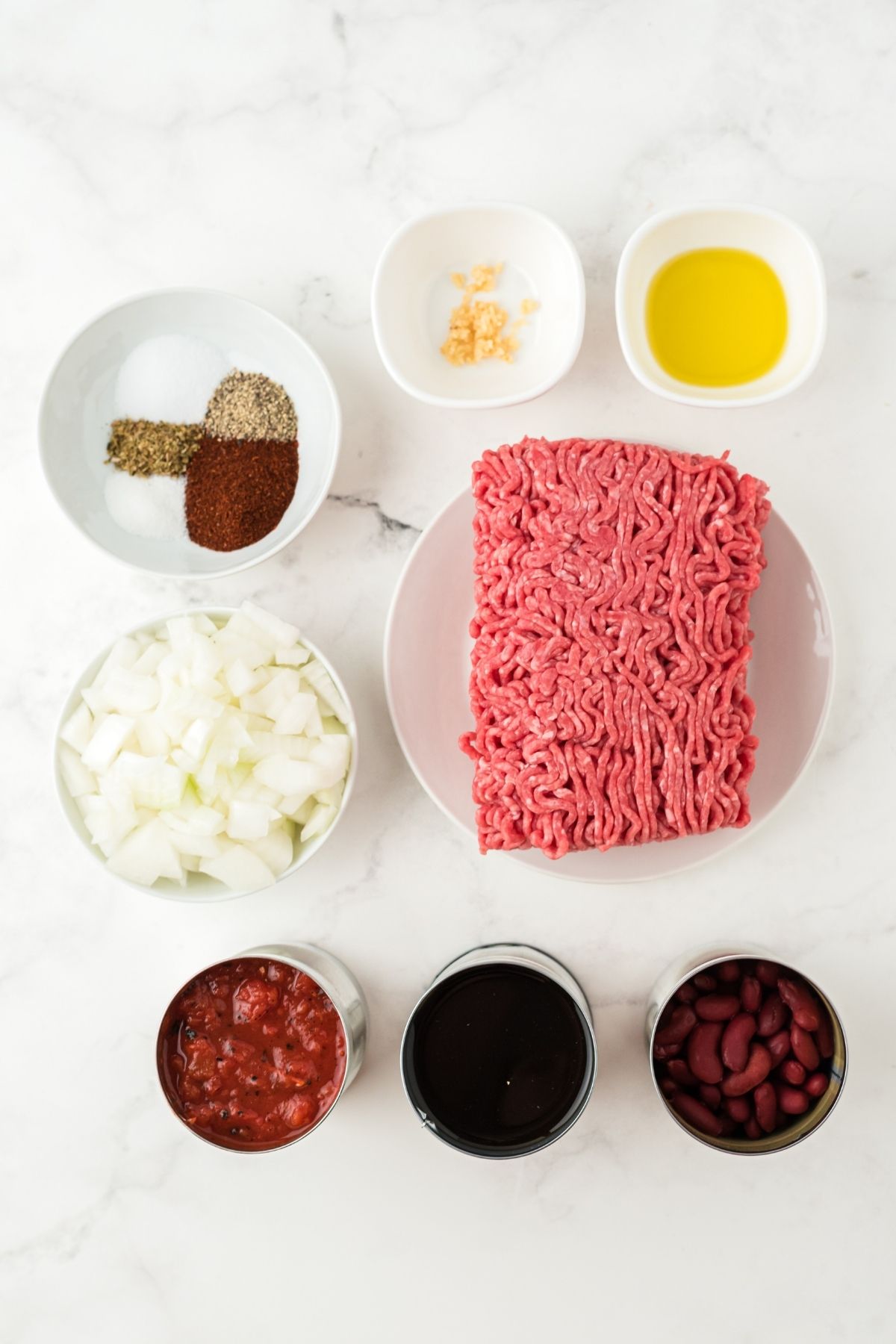 ingredients on counter: ground beef, bowl with seasonings, chopped onion, olive oil, red kidney beans, crushed tomatoes in can, broth, Worcestershire sauce, sugar