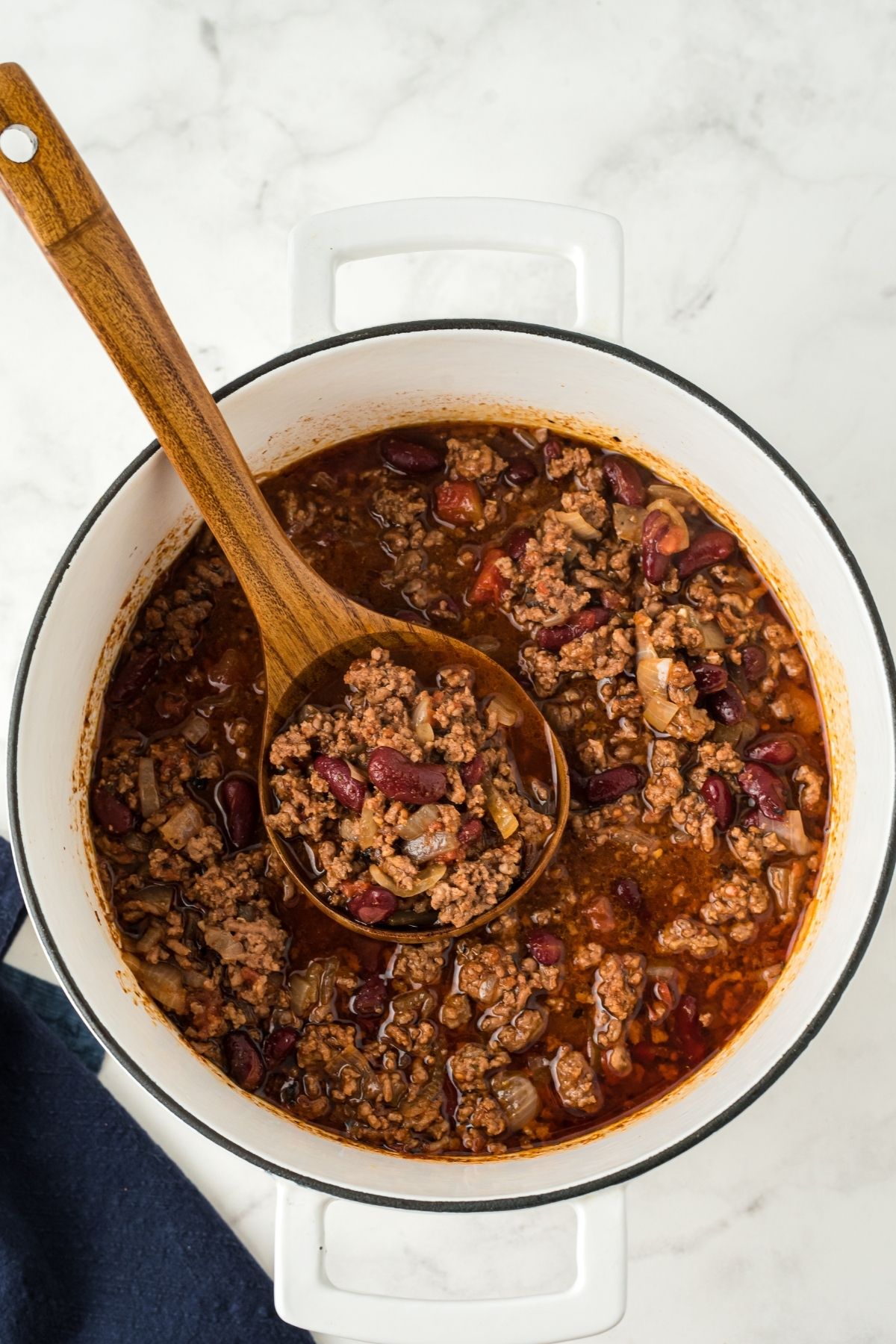 large stock pot with cooked chili and a wooden ladle