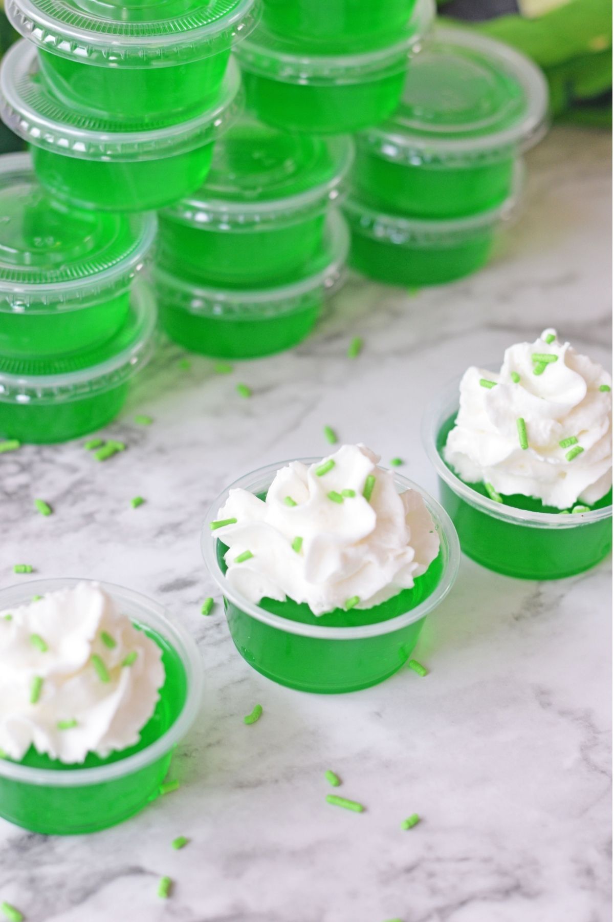 green jello shots in plastic cups with whipped cream and lime green sprinkles