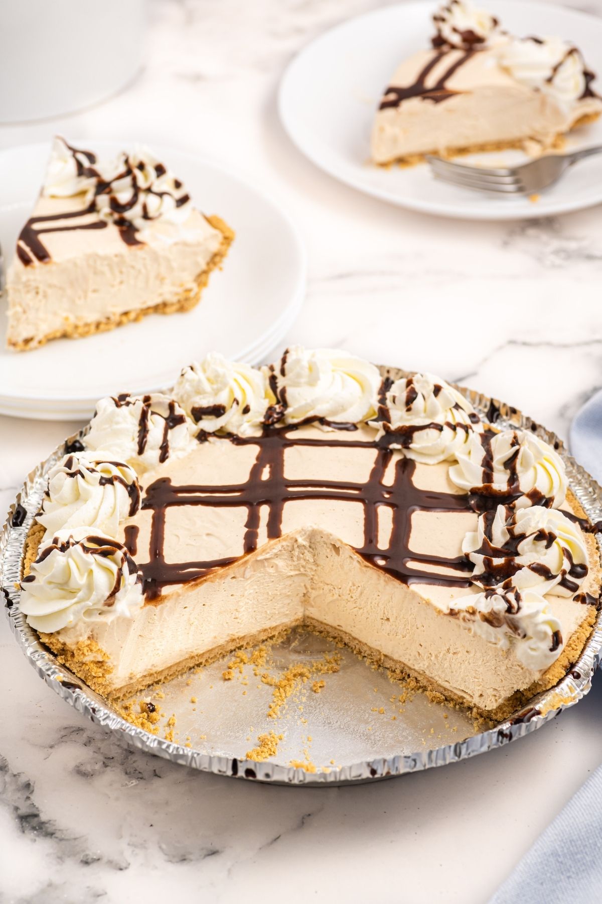 peanut butter pie with two slices taken out showing the inside smooth edges, whipped cream around edge with criss cross chocolate on top