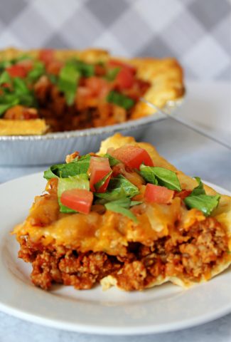 Taco bake slice on a plate with salad leaves and chopped tomato on top.
