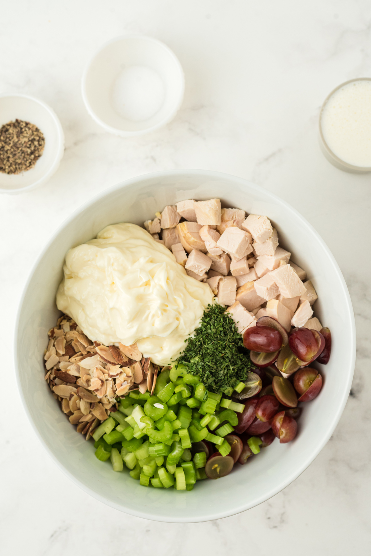 Combining all ingredients of Neiman Marcus Chicken Salad in a white bowl.