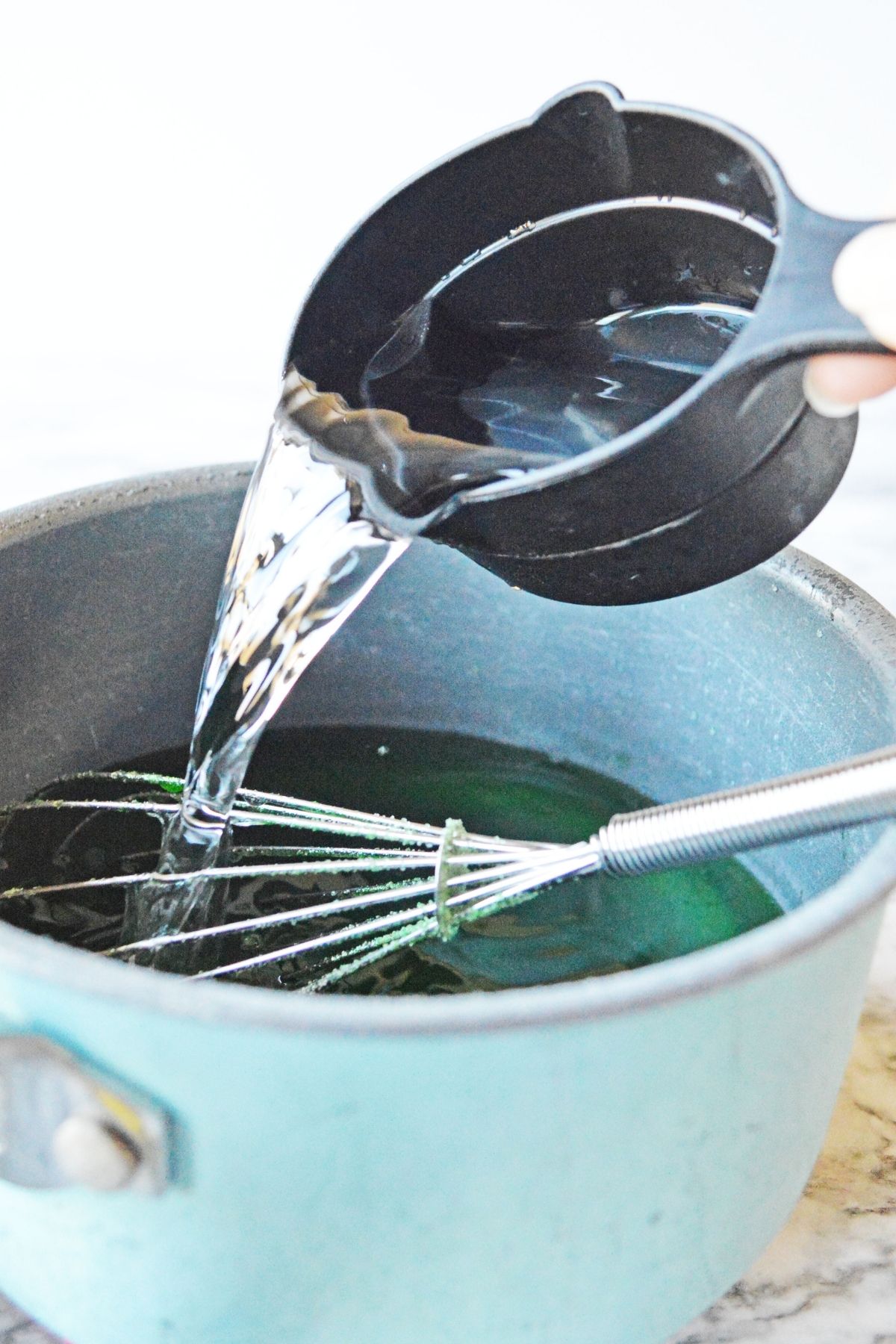 measuring cup pouring cold water into green jello