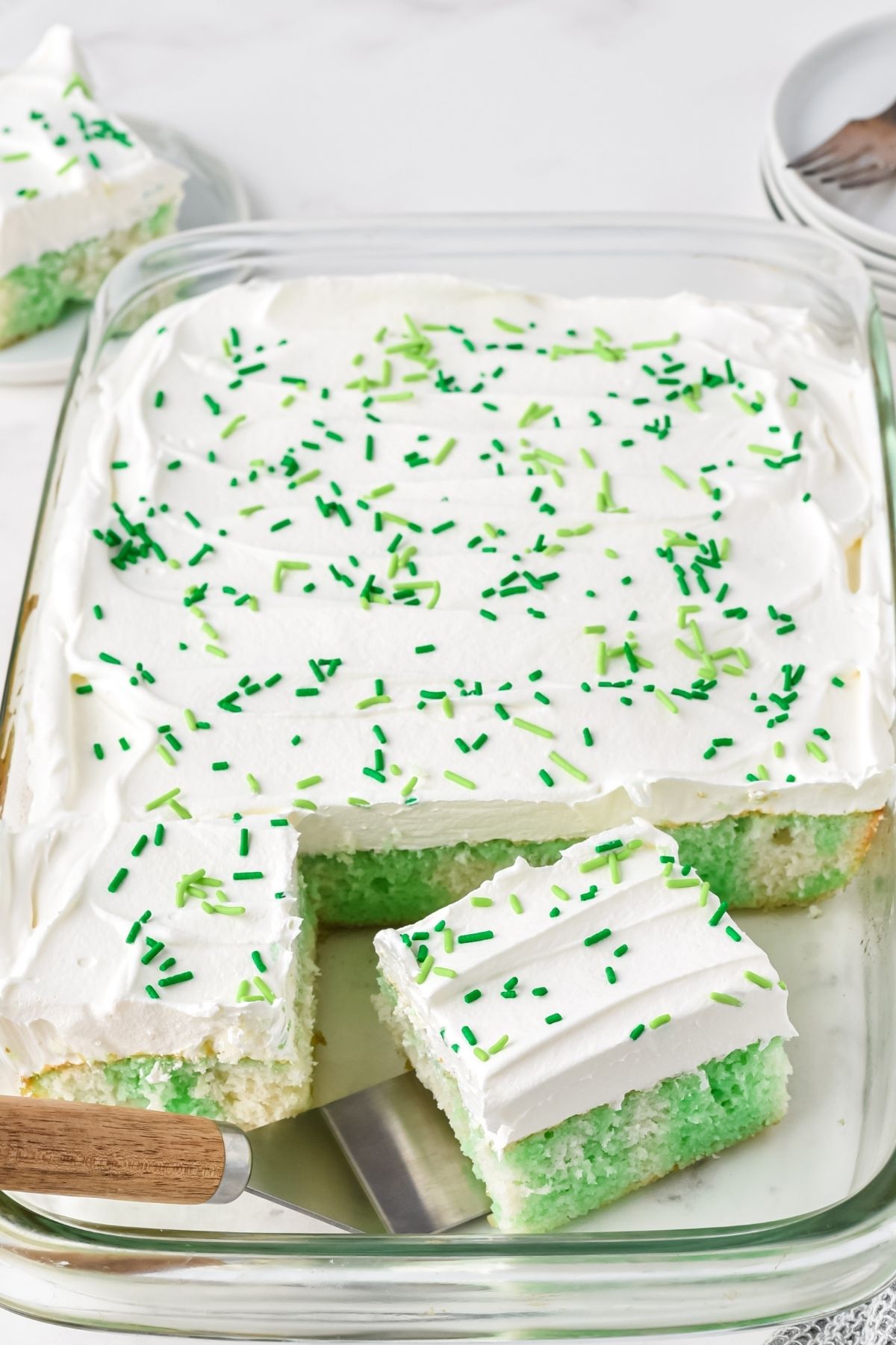 green and white cake in 9x13 pan with white frosting and green sprinkles