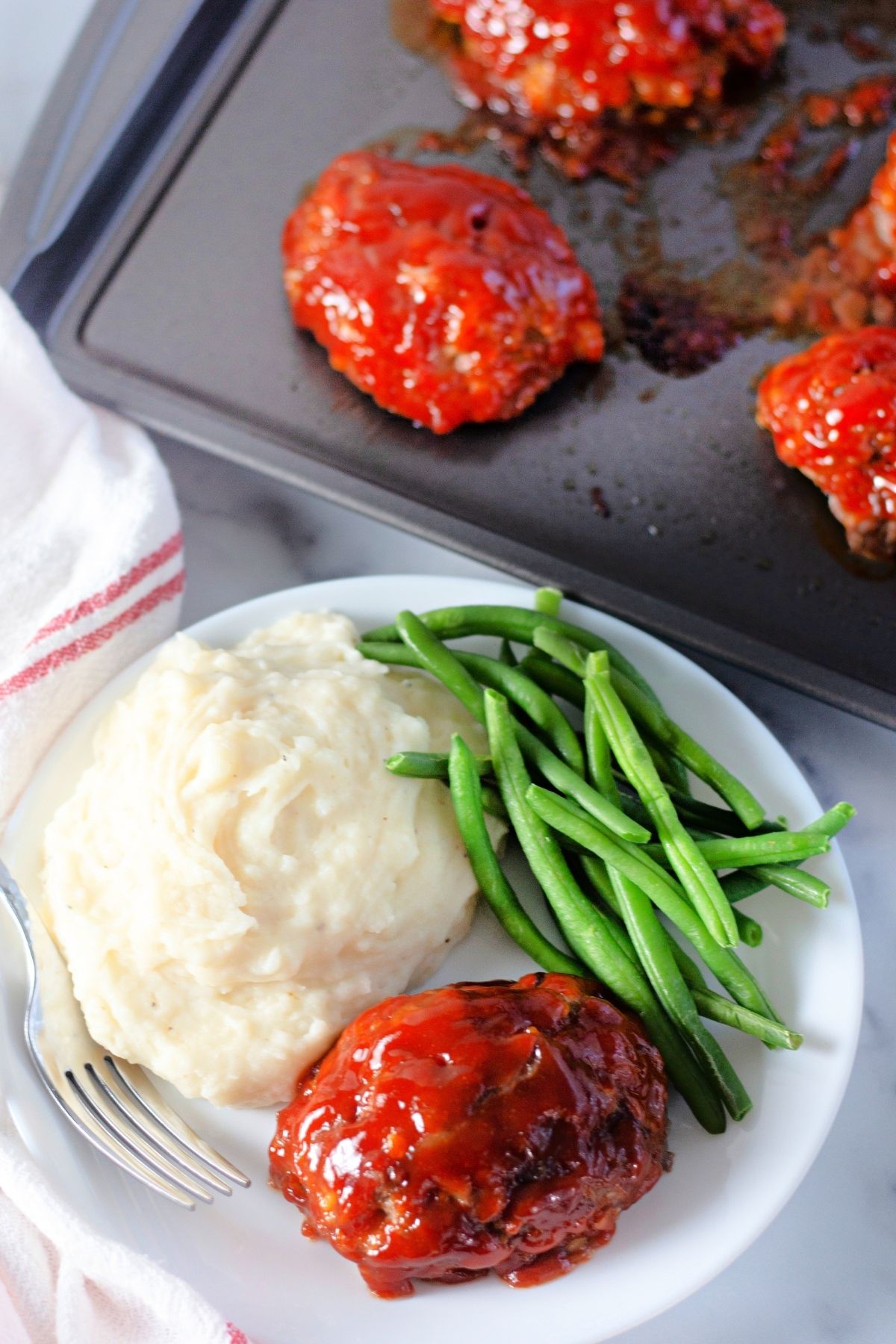 small meatloaf on plate with green beans and mashed potatoes