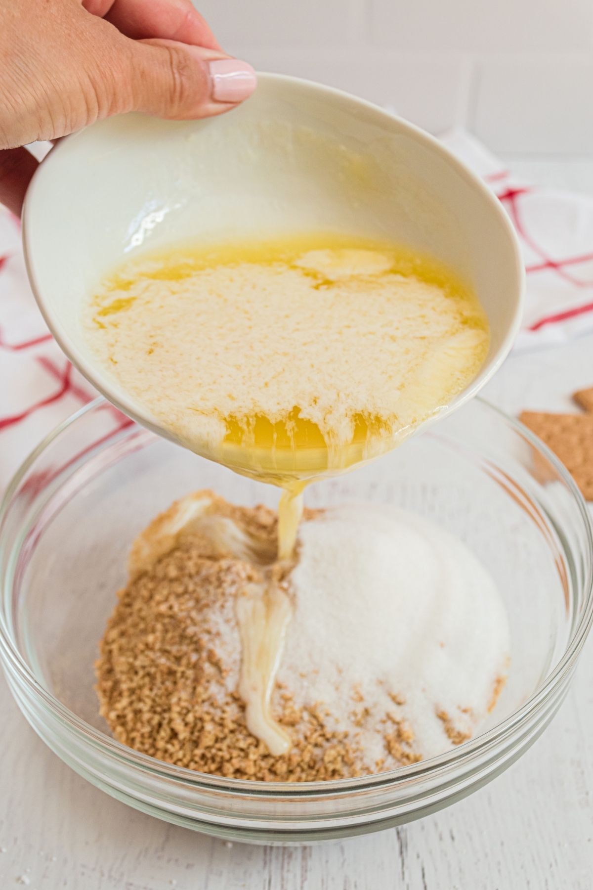 pouring melted butter into bowl with crushed graham crackers and sugar