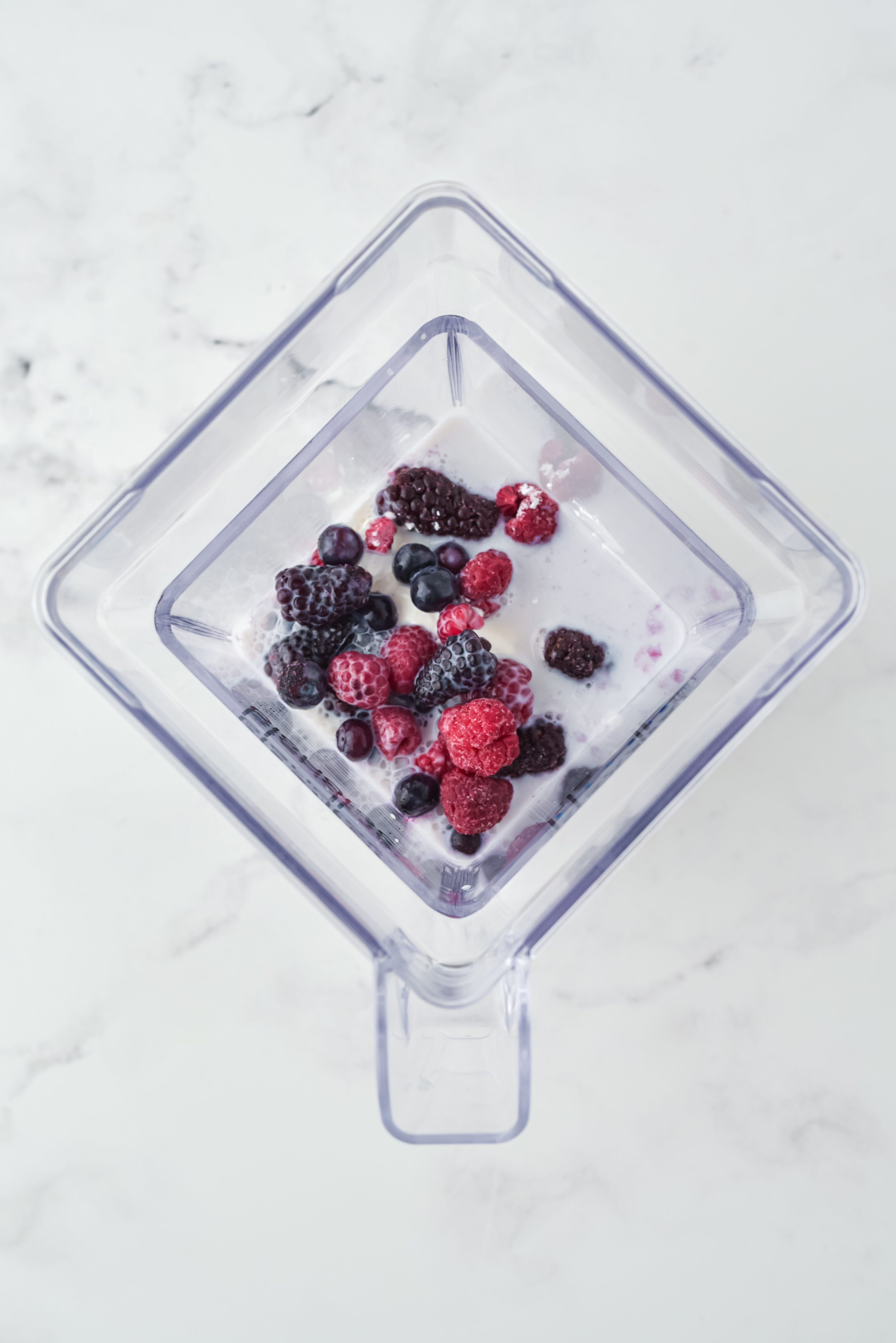 Top view of blender with frozen berries, yoghurt and cool whip in it. 