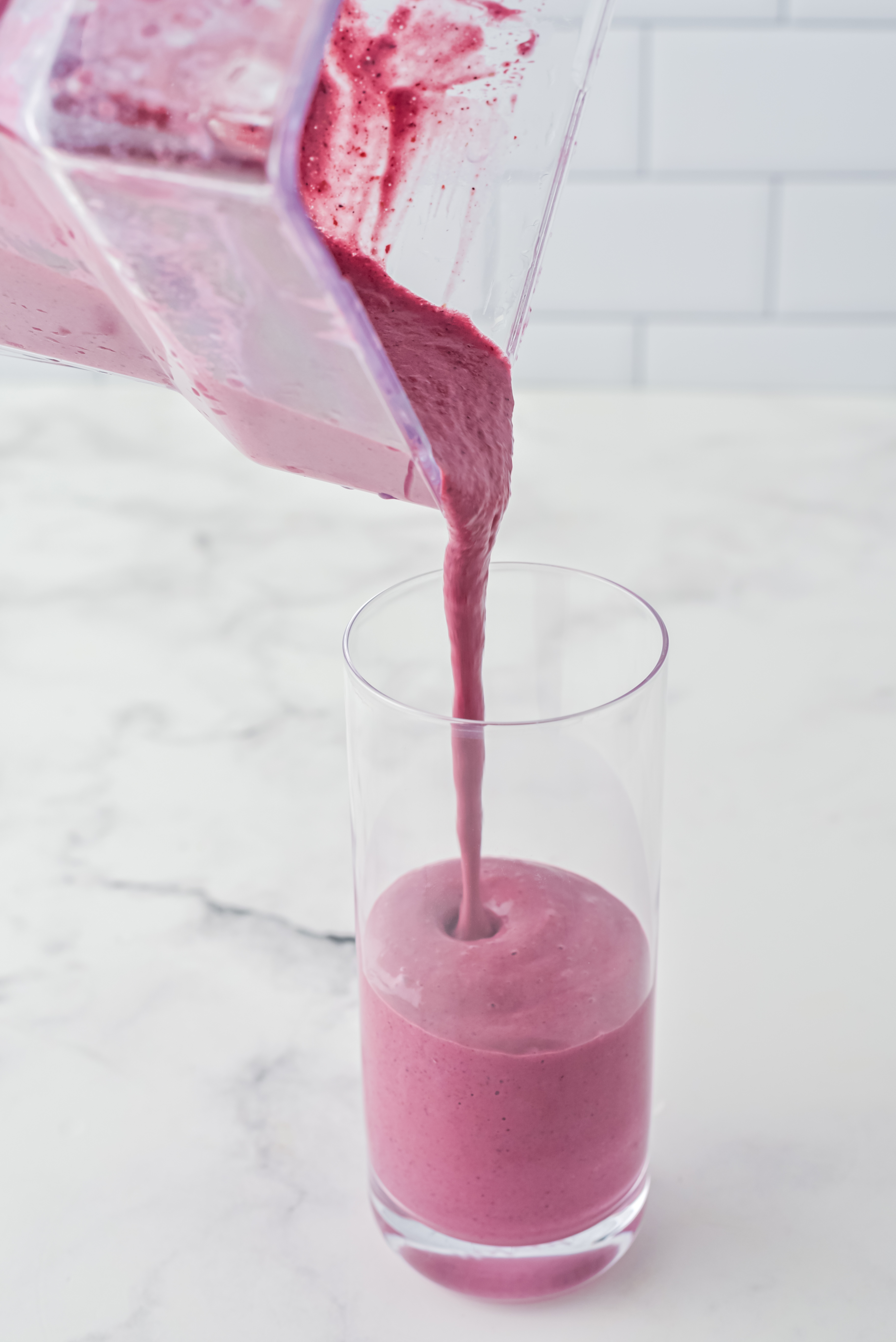Pink Smoothie mix being poured into a glass on a white counter. 