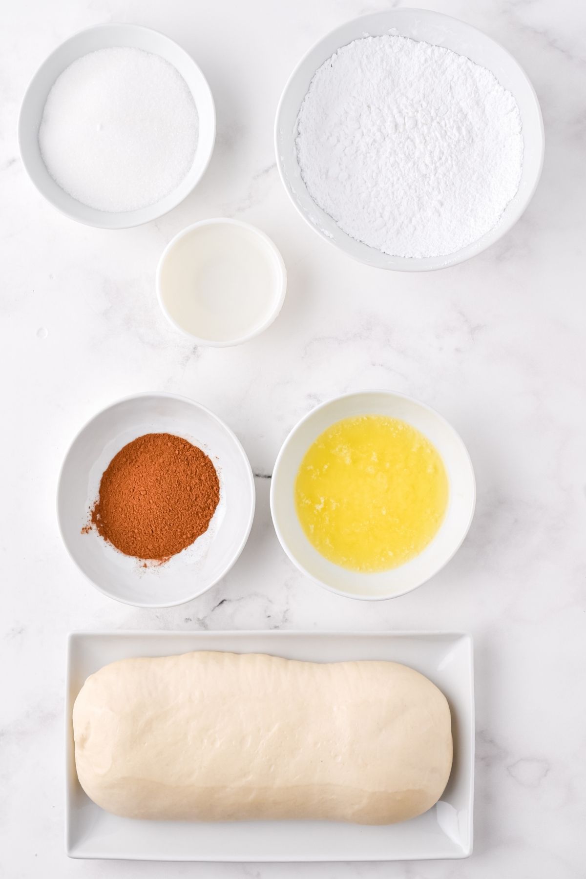 ingredients on white counter: cinnamon, sugar, frozen bread loaf, powdered sugar, water