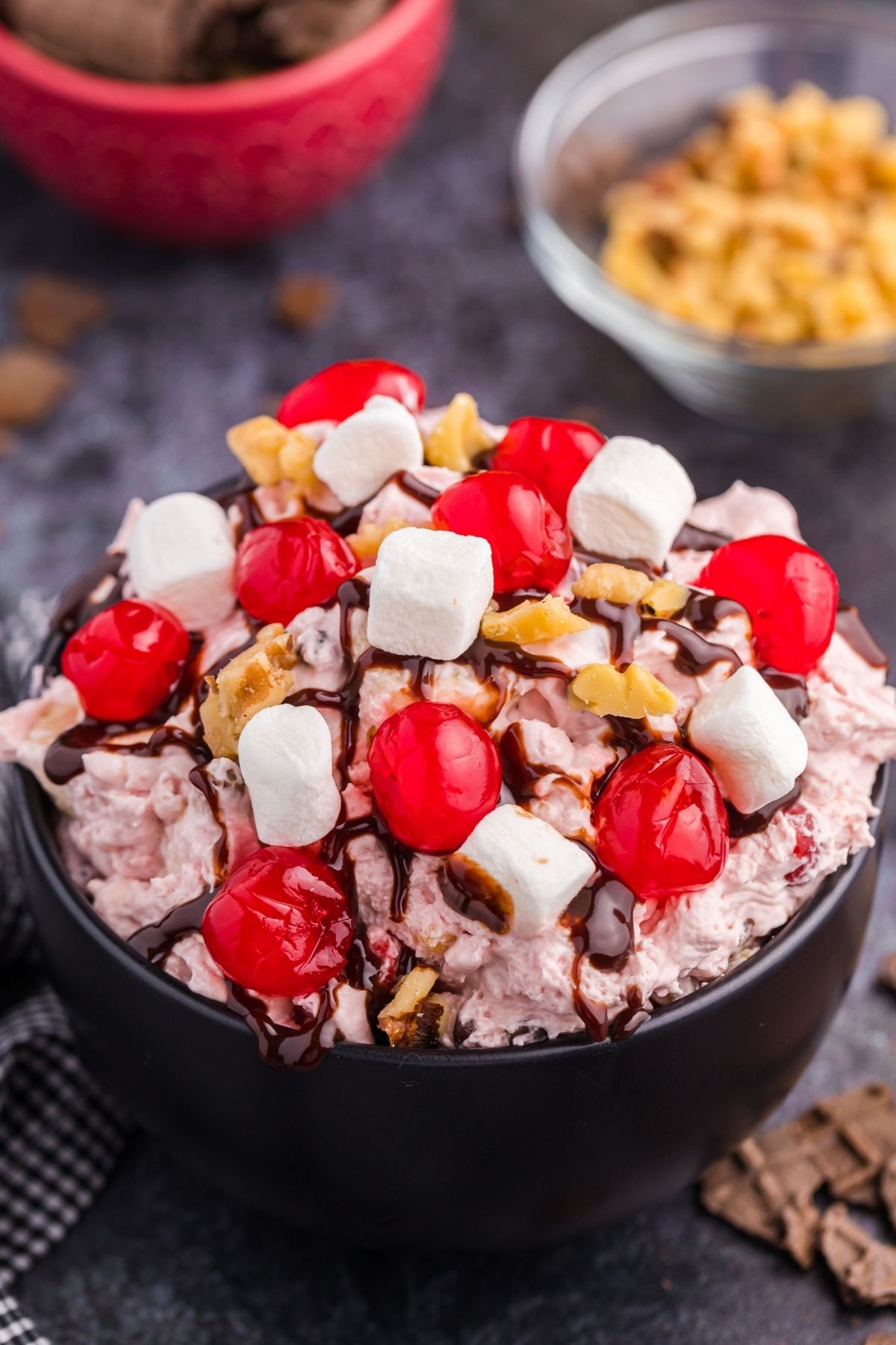pink fluff in dark bowl with maraschino cherries, mini marshmalllows and chocolate sauce on top