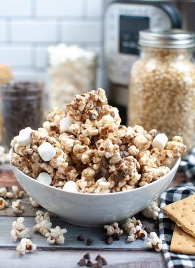 Popcorn and mini marshmallows in a white bowl on a kitchen counter top, covered in chocolate.