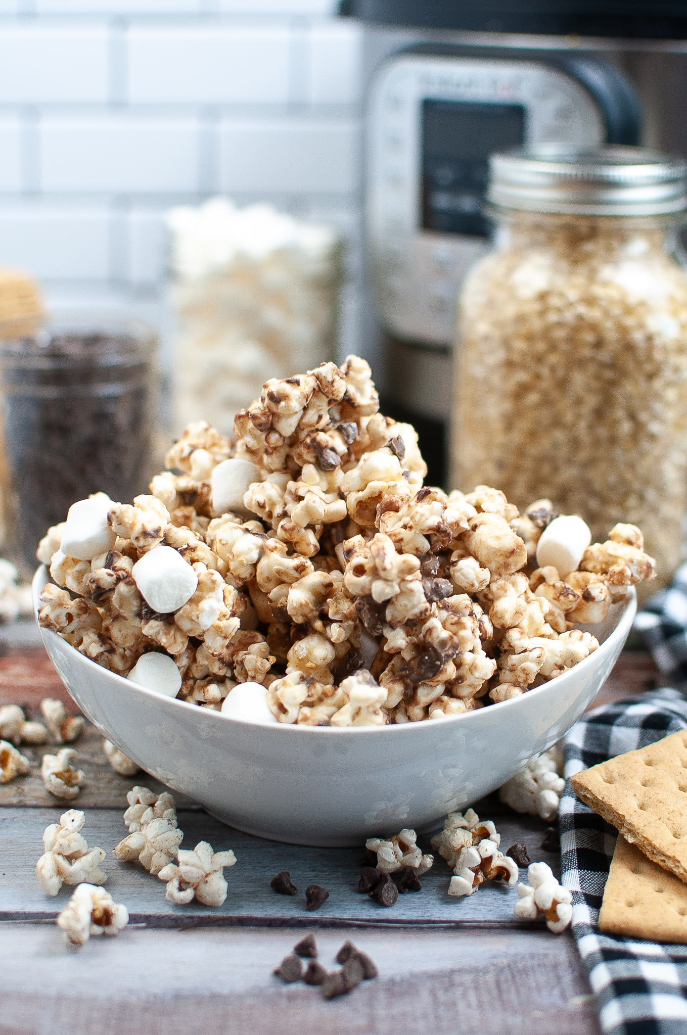 Popcorn and mini marshmallows in a white bowl on a kitchen counter top, covered in chocolate.