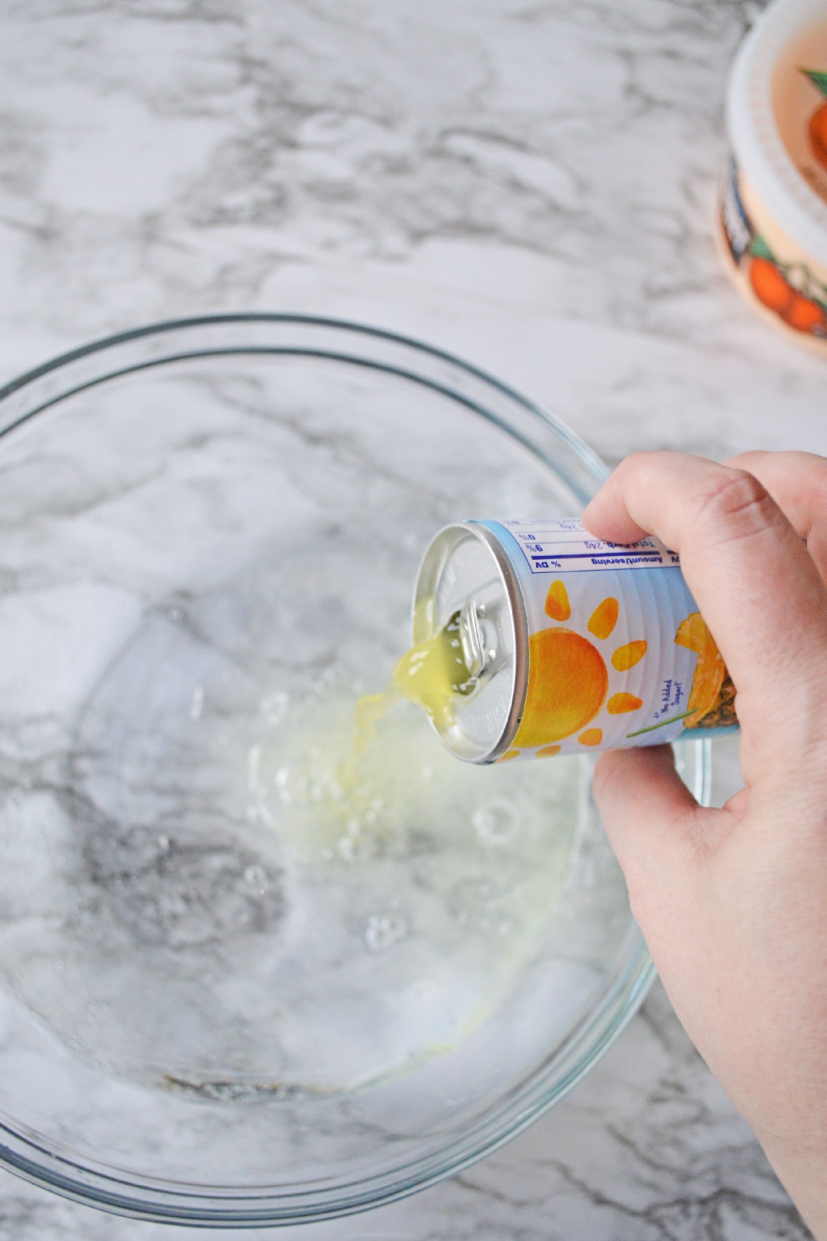A can of pineapple juice being poured into a large punch bowl with Sprite in it.