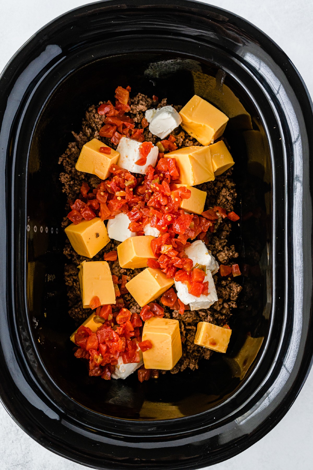Cheese and chillies on top of beef in a Crockpot. 