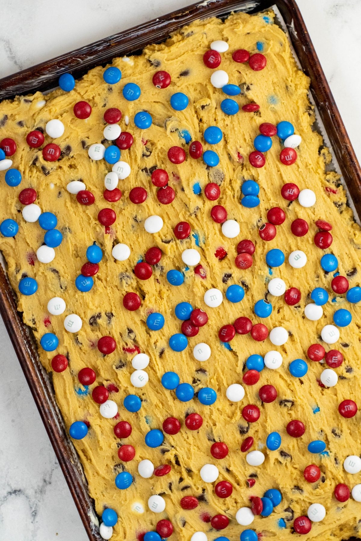 cookie dough spread out on baking sheet with M&Ms on top