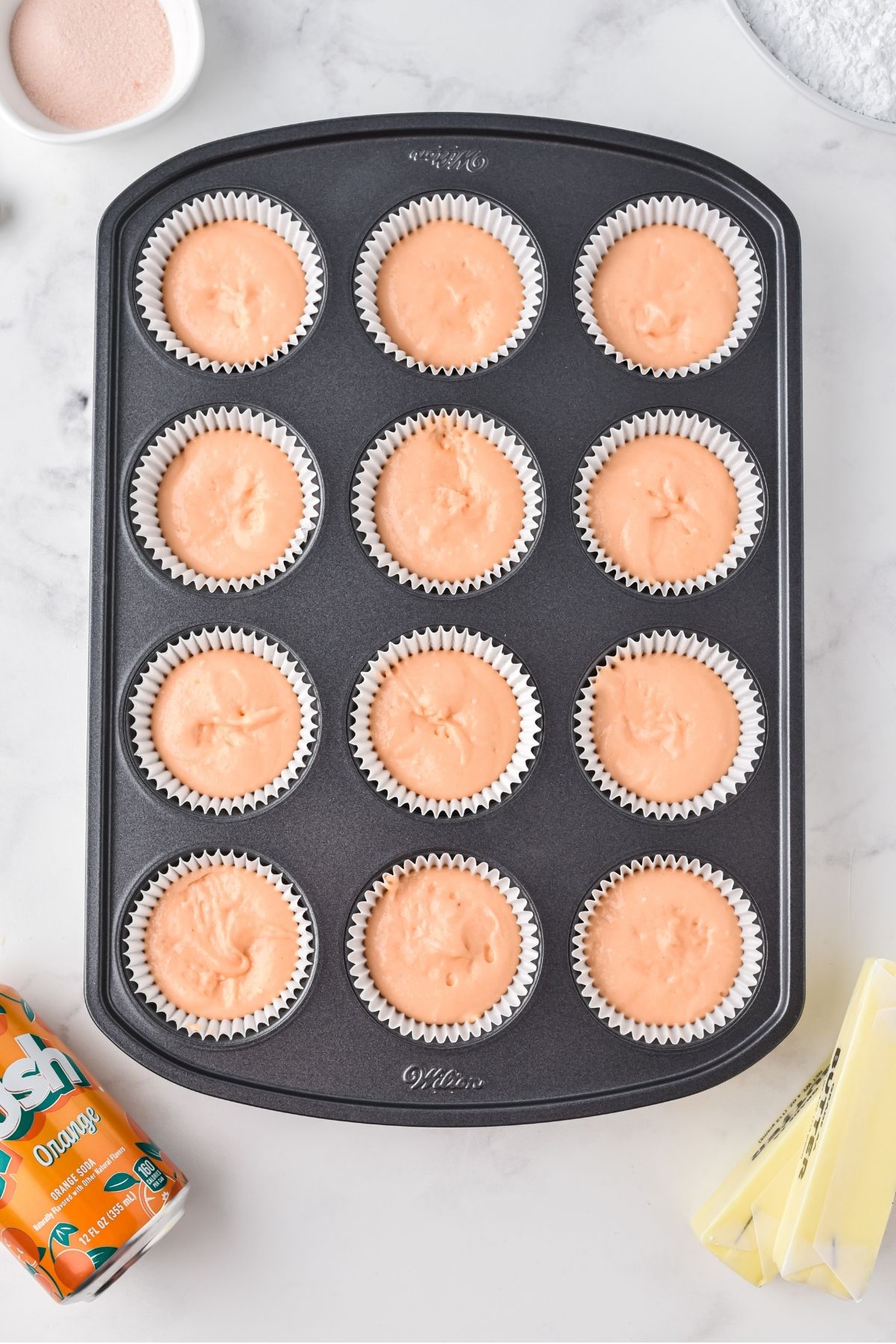 cupcake pan with 12 cupcakes with orange batter and white liners