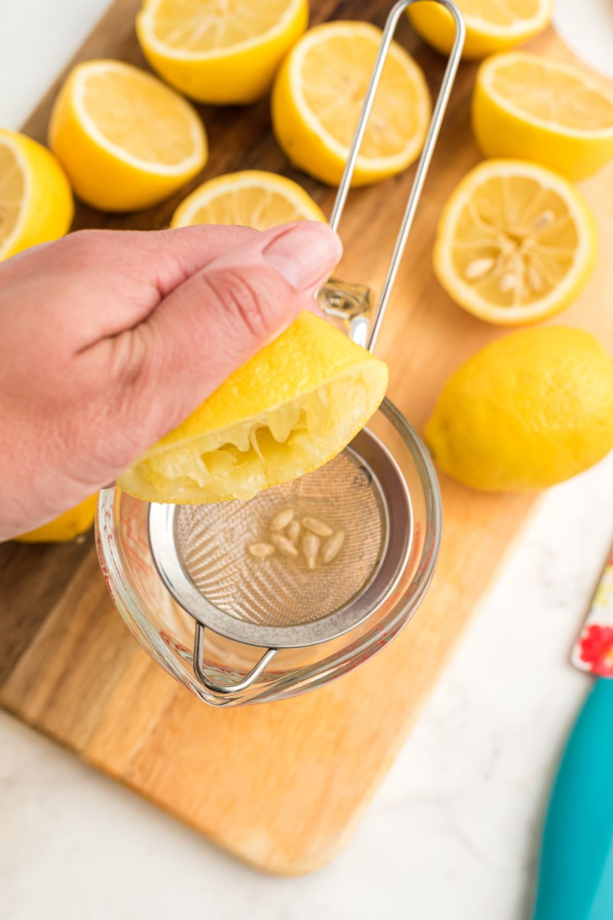 hand squeezing lemon into glass measuring cup with strainer catching seeds