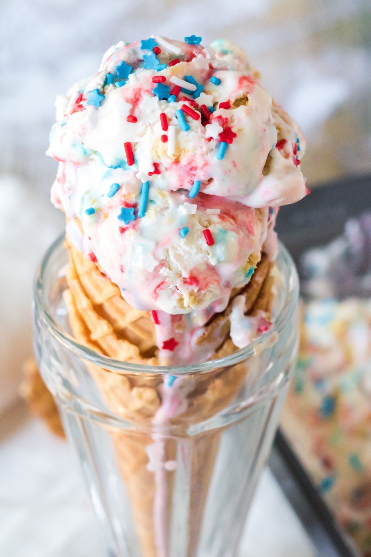 ice cream cone with a couple of scoops of red, white, and blue ice cream standing up in a clear glass