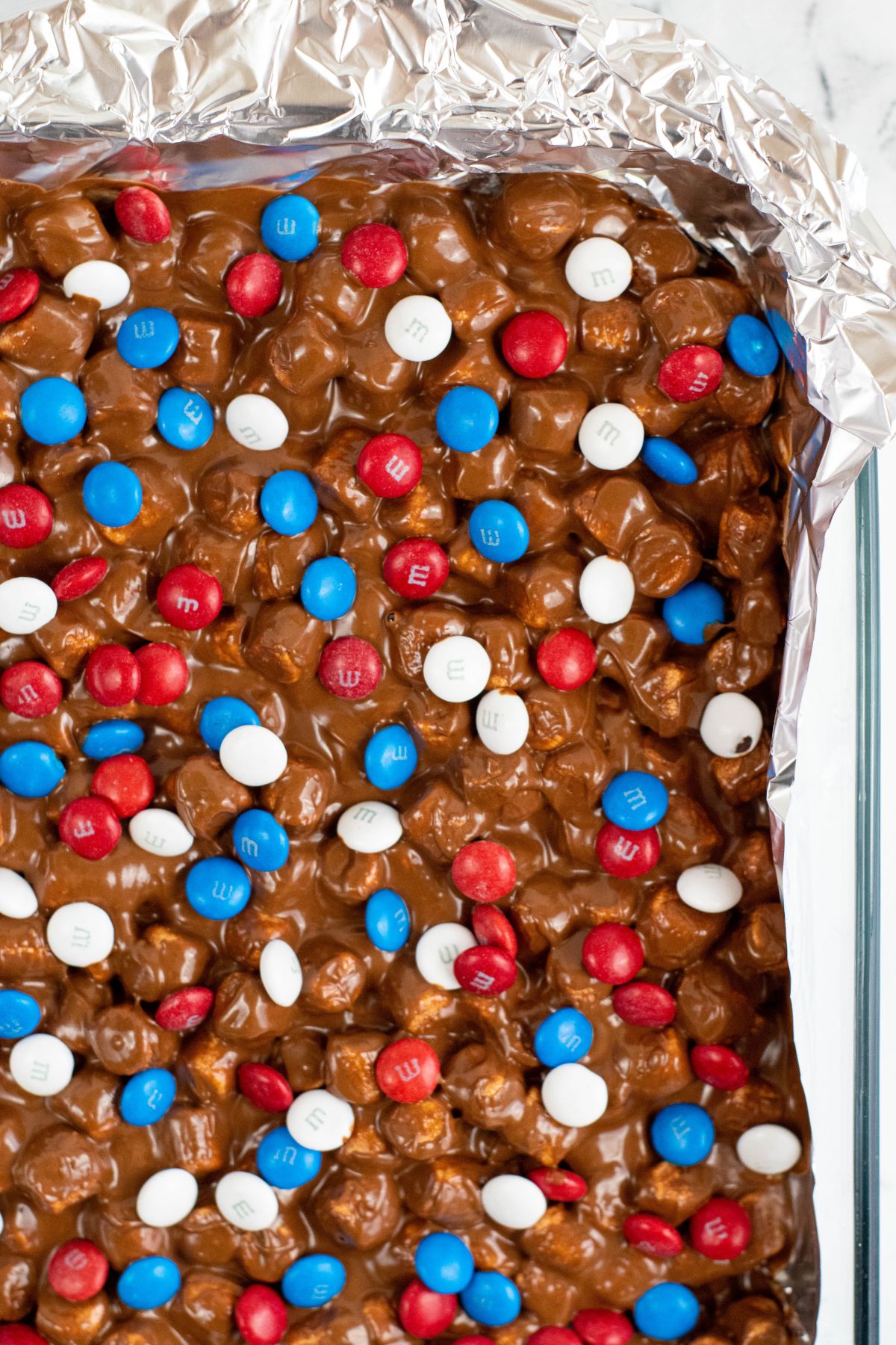 red, white, and blue M&Ms on top of melted chocolate with marshmallows in pan