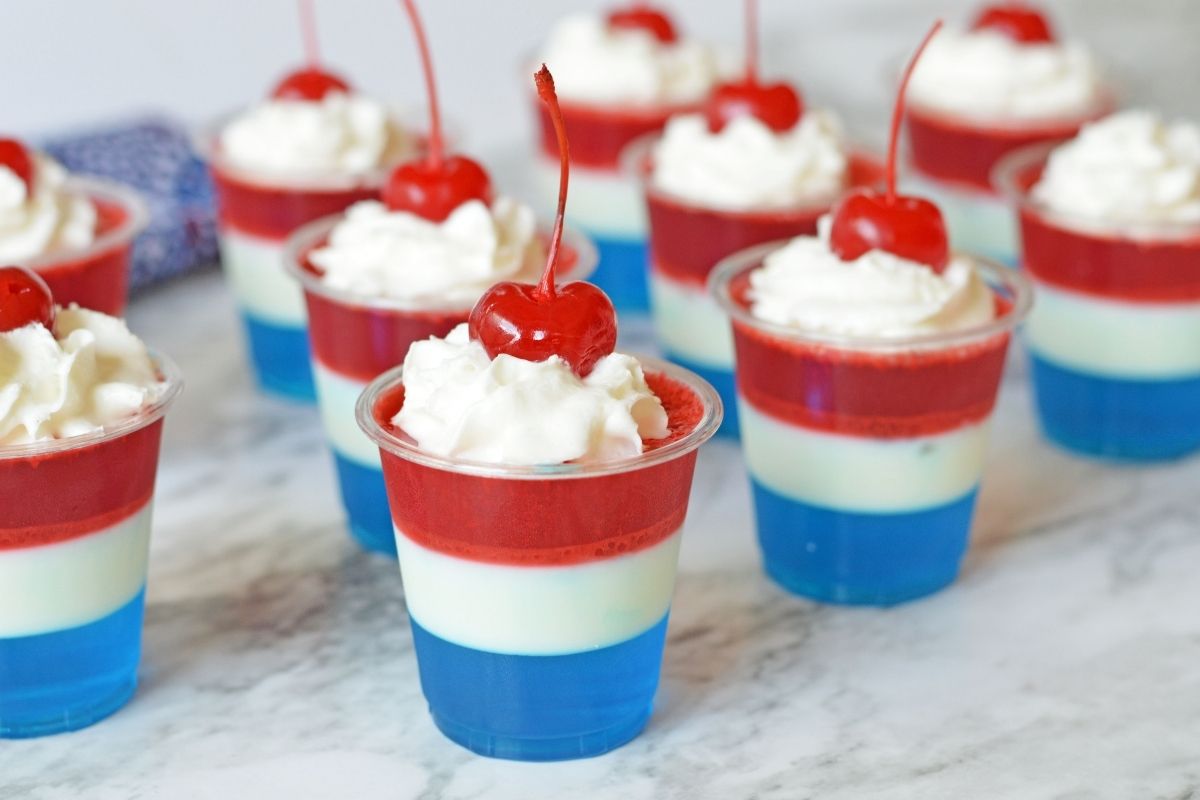 jello shots lined up and topped with whipped cream and maraschino cherries