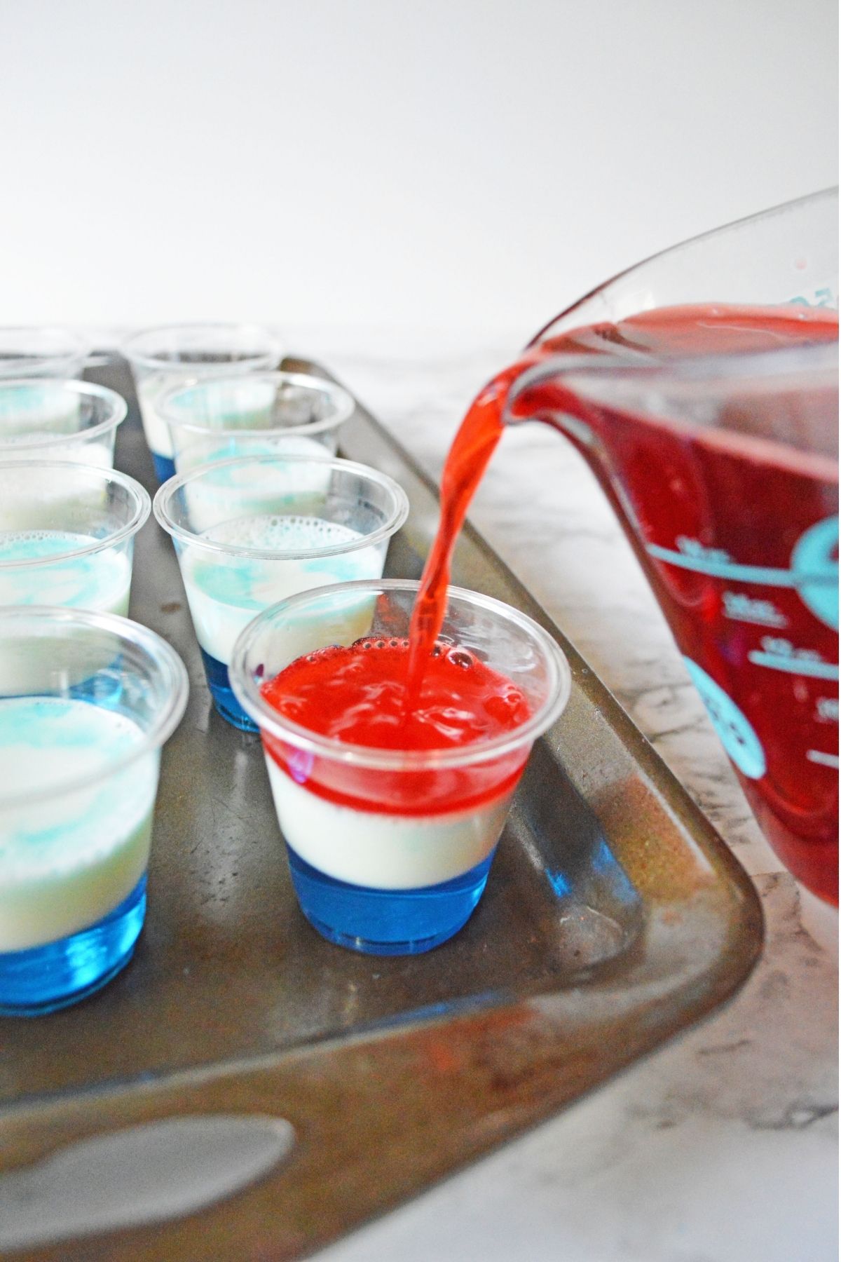 pouring red jello on top of white layer in small cups